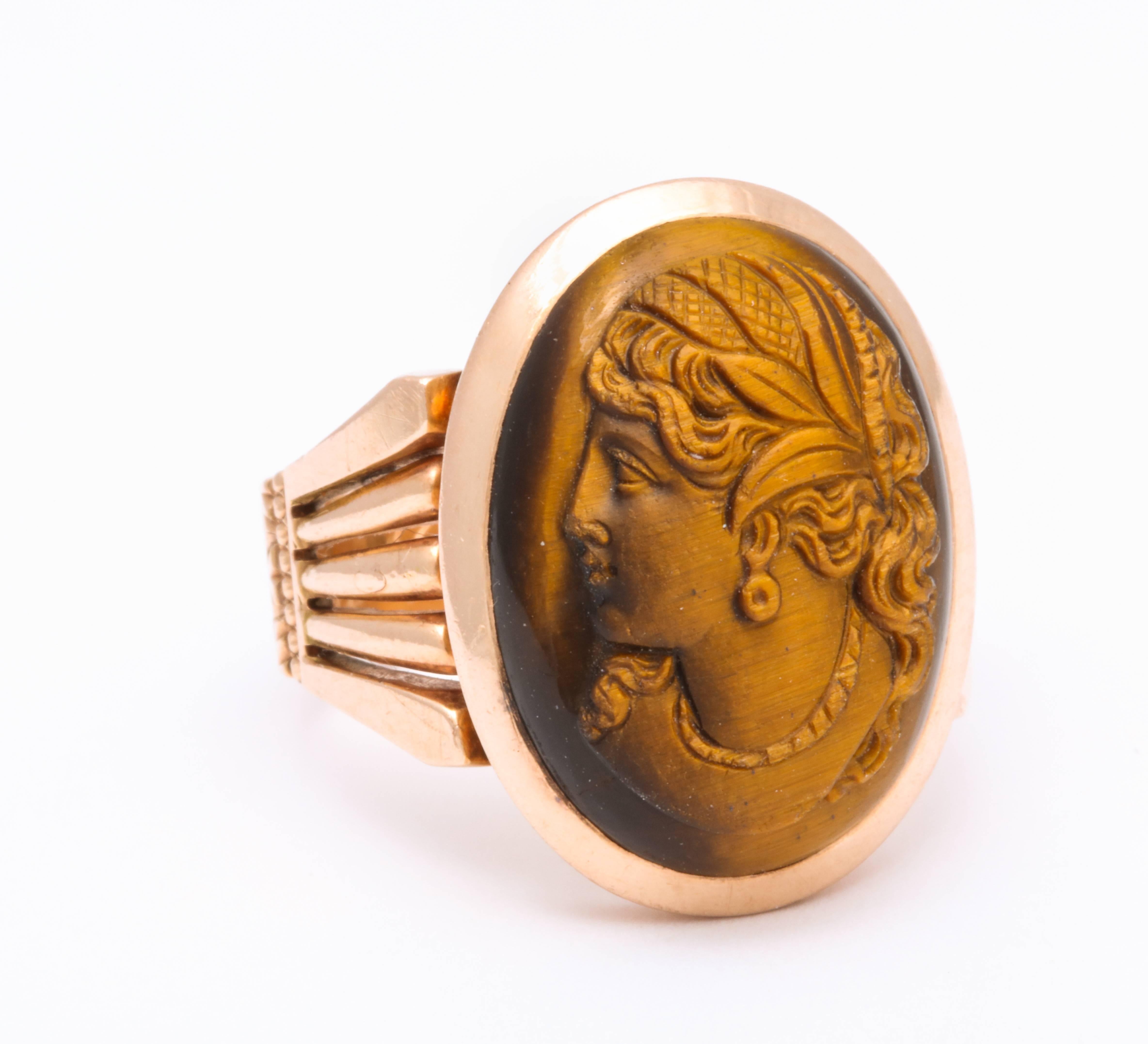 A substantial shank of 14 kt gold holds a gem tiger eye stone cameo of a sensuous classical woman, wearing a diadem engraved in crosshatch. The stone of two colors, carved to perfection in left profile, brings the golden woman forward flashing in