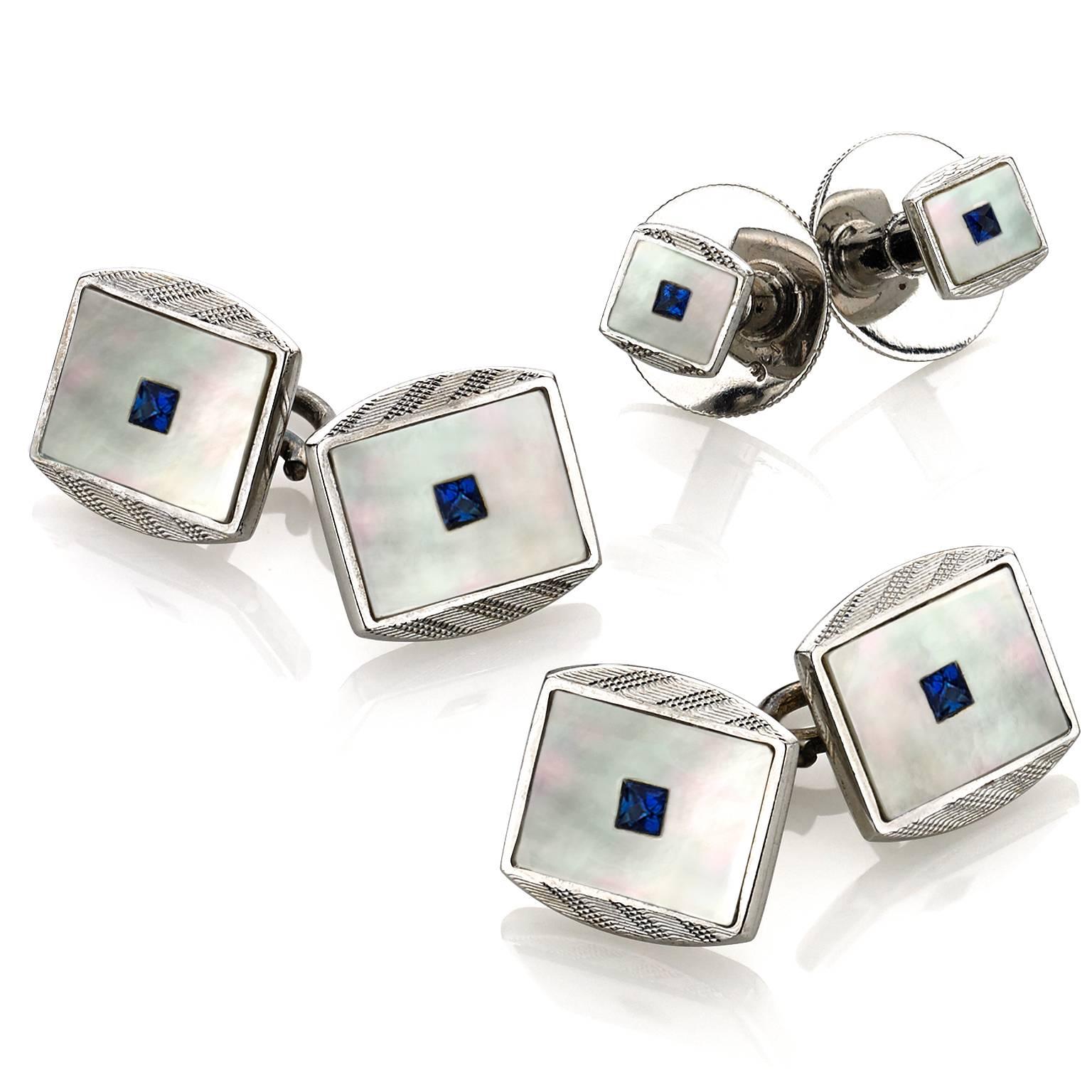 British Dress Set (cuff links and stud set) in 9k white gold with princess-cut blue sapphire and mother-of-pearl, circa 1915. 

Four Screw-Back Button Studs
Two Double-Sided Cuff Links