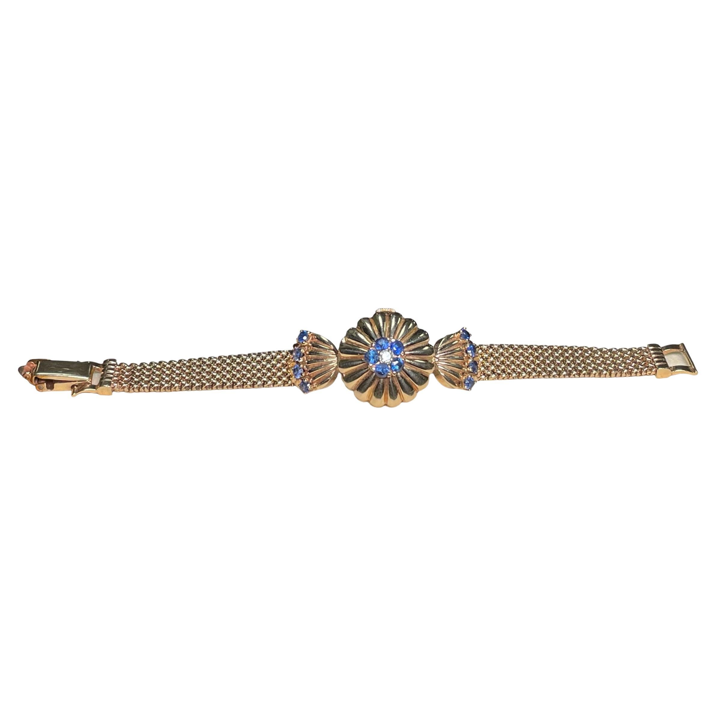 This is a 14K Gold, Diamond and Sapphires Watch Bracelet. It depicts a hidden round watch (Frankfurt 17 jewels manual wind movement) with a gold lid cover shaped as a flower with reeded petals and embellished in the center with five sapphires in