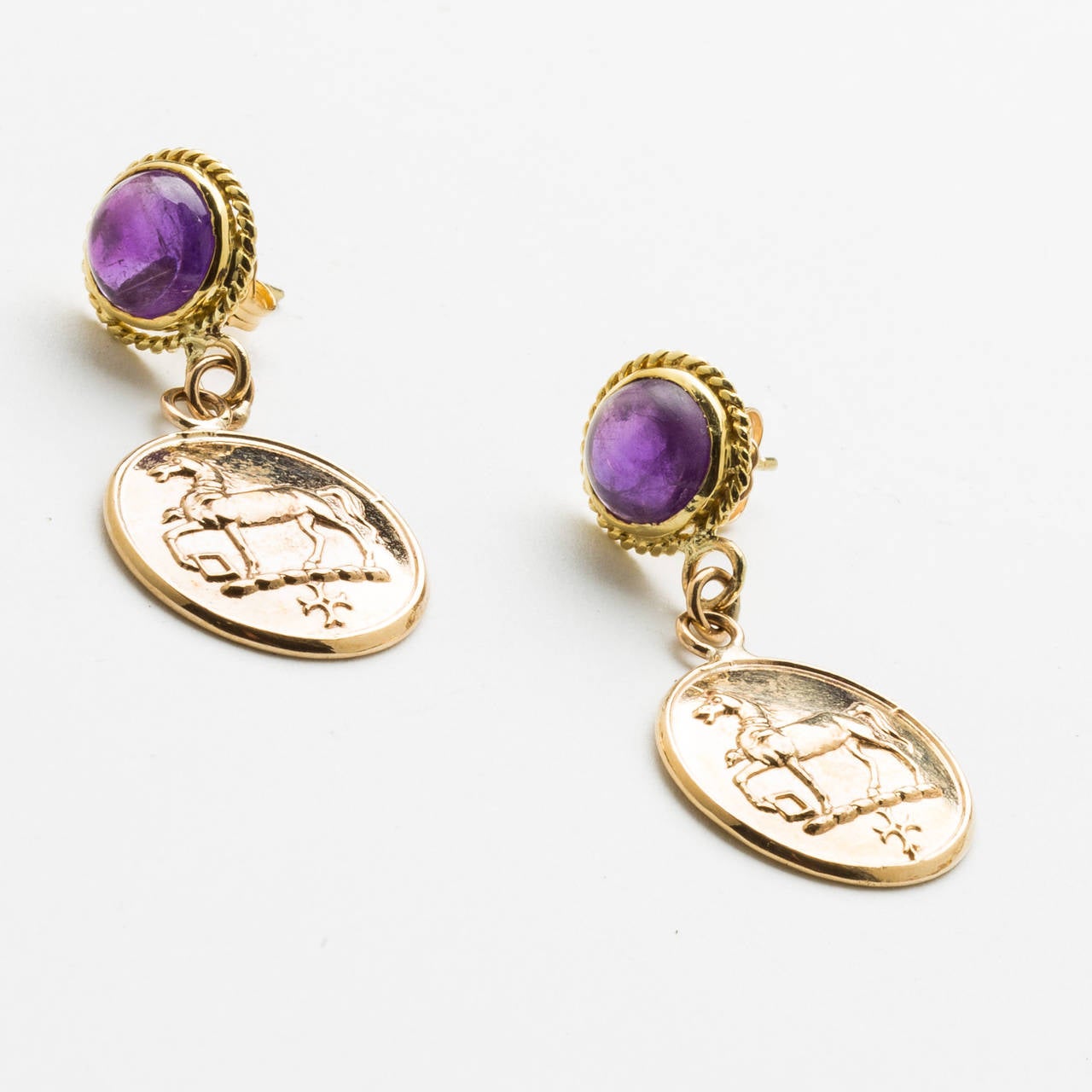 A pair of lovely 10 karat rose gold stamped equestrian coin earrings, in low relief, dangling from round amethyst cabochons studs set in twist wire 18 Karat yellow gold frame. For pierced ears. Coins 18mm round & amethyst cabochons 8mm round.