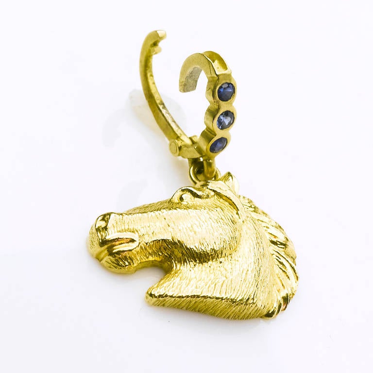 Hand crafted horse head pendant in profile with flowing mane in18Karat polished yellow gold (26mmx20mm) set with bright blue sapphire (.30cts) detachable bail.