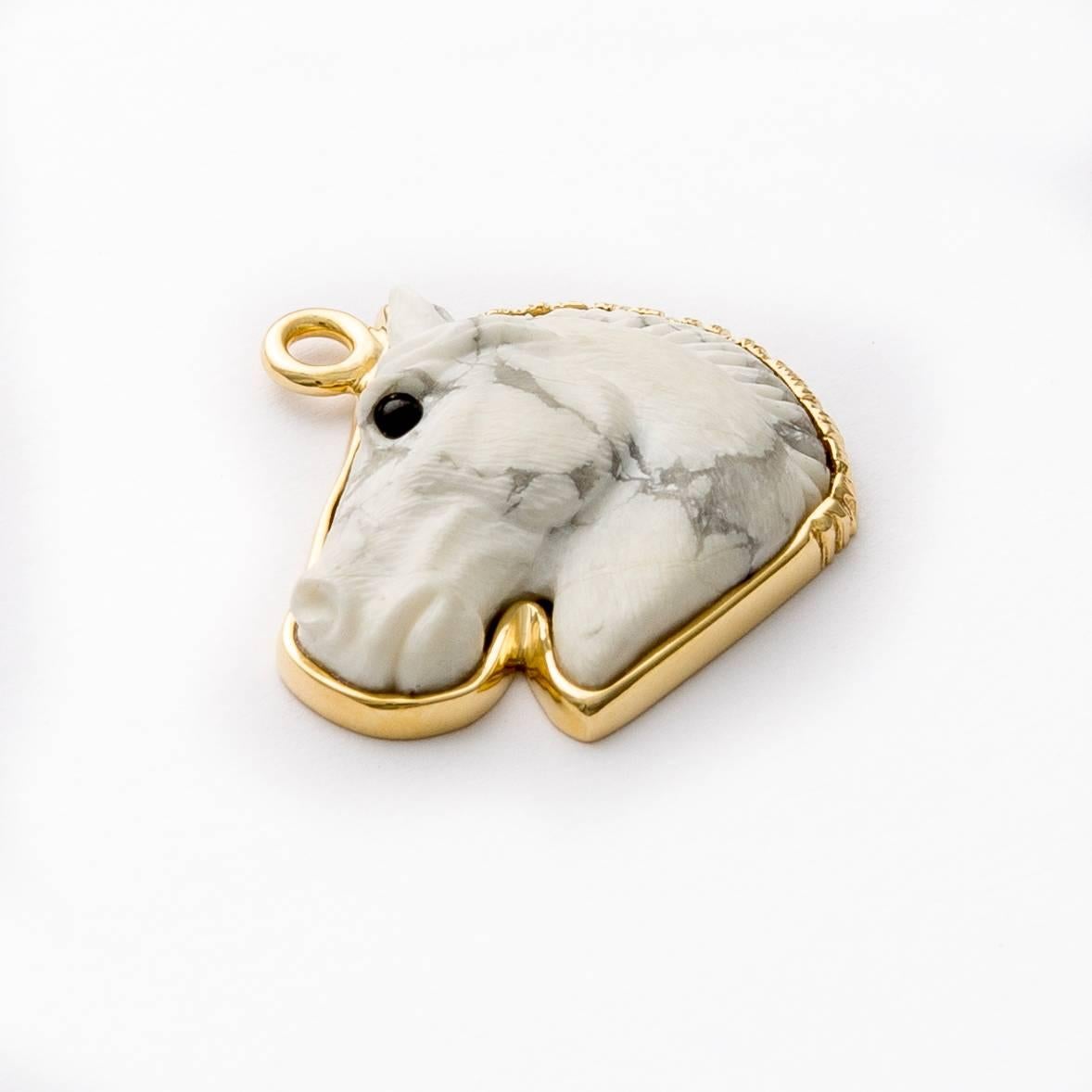 Hand carved howlite horse head pendant with onyx eye in profile set in 18 karat brushed gold frame with loop (carved by Master Idar-Oberstein artist). 
Stone: Natural howlite with light grey veining, size: 28mmx22mmx5mm.
Gold detachable enhancer