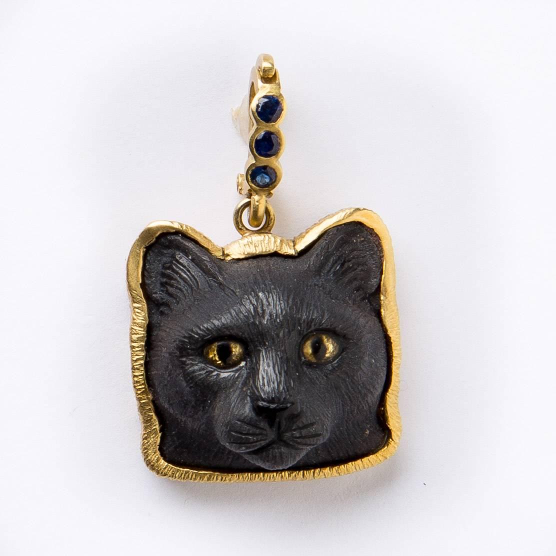 For cat lovers here is a beautifully hand carved obsidian cat's head pendant with crystal painted eyes set in an 18 karat gold frame with .30 carat blue sapphire enhancer which opens to hang from your necklace. 24mmx24mmx14mm stone size. Created by