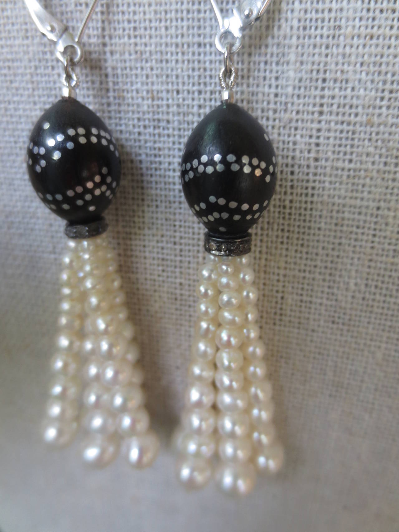 These elegant earrings feature graduated pearl strands suspended from antique bead caps. The dark caps are made of wooden beads with silver nail inlay design and are accented with a diamond encrusted sterling silver rondelle at the base. Ear-wires