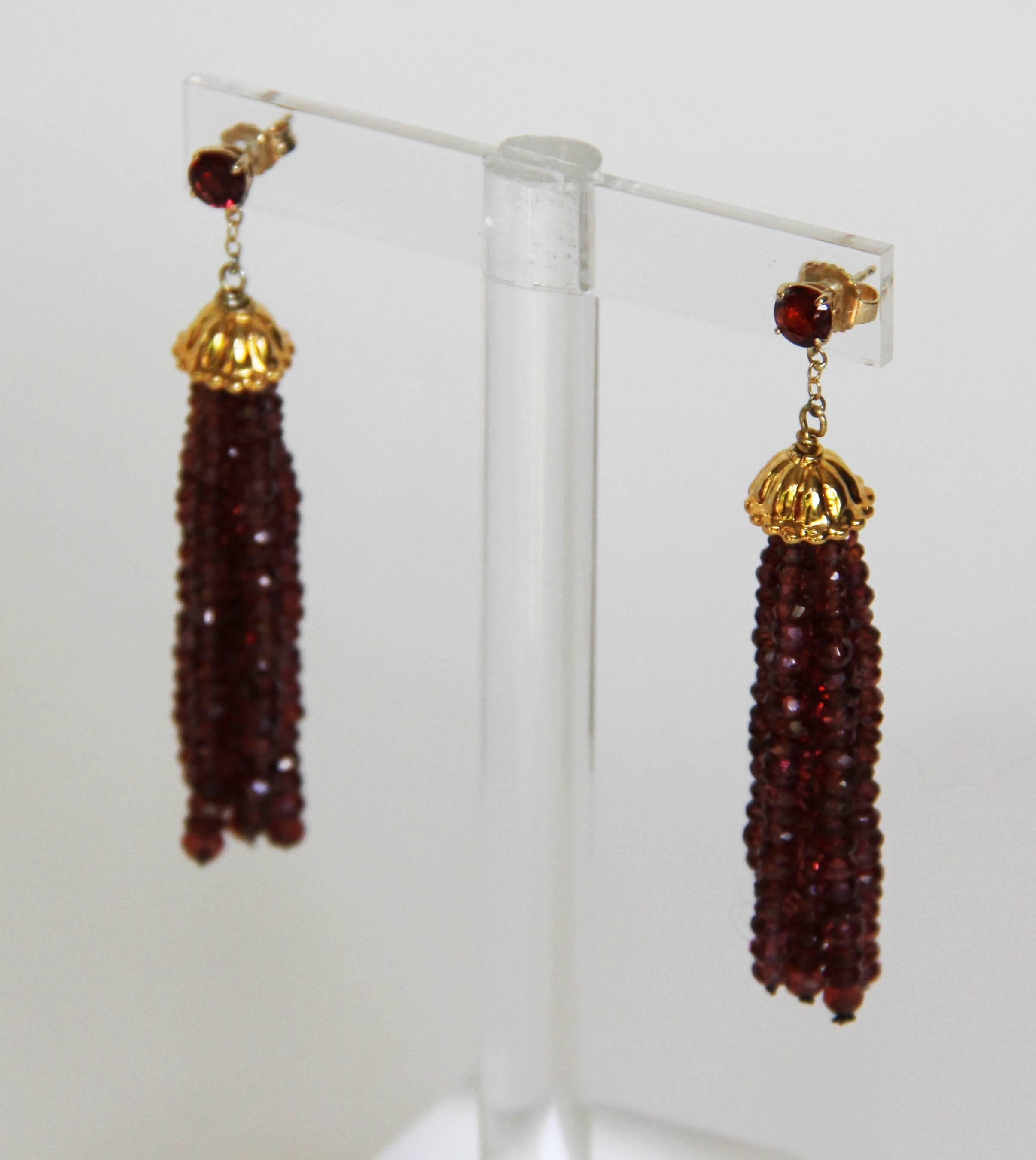 Rich deep burgundy faceted garnet beads hang in graduated strands from a gold plated silver corrugated cup. A 14k yellow gold chain connects the tassel to a .5 mm opulent red garnet stone and 14k yellow gold stud. These earrings hang at 2.25 inches,