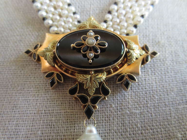 This exquisite necklace is made from a unique centerpiece, originating from a black onyx Victorian brooch. The delicate centerpiece is ornamented with antique pearls, and set within a 14k gold ornate frame detailed with onyx. The pearl necklace is