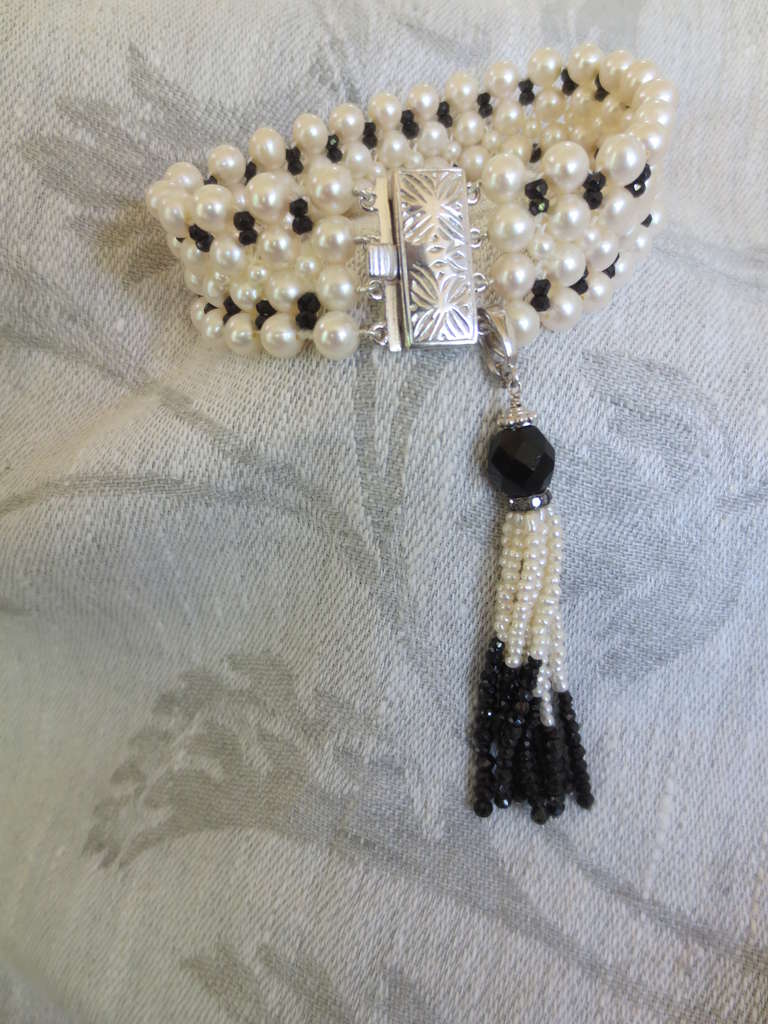 This inspired woven pearl and onyx bracelet with tassel and 14k white gold clasp is inspired by Art-Deco jewelry. Elegant hand woven 3 mm and 5 mm pearls and faceted onyx beads meet at a rhodium plated sterling silver clasp with a elegant floral