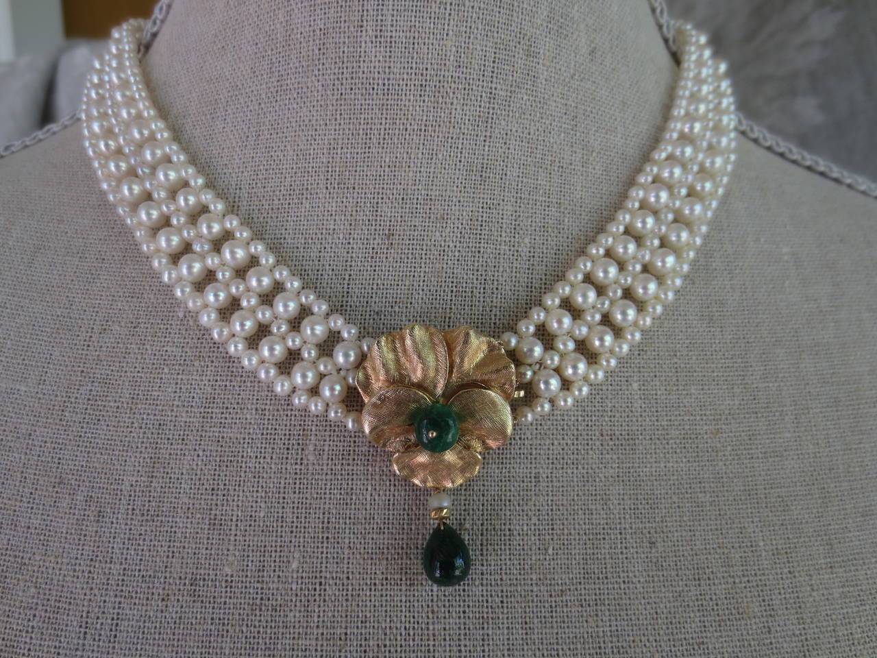 This handwoven white pearl necklace with emerald and 14 k yellow gold floral centerpiece is beautiful and practical as the centerpiece acts as a front-facing clasp. The floral design centerpiece is made of 14 k yellow gold petals with a central
