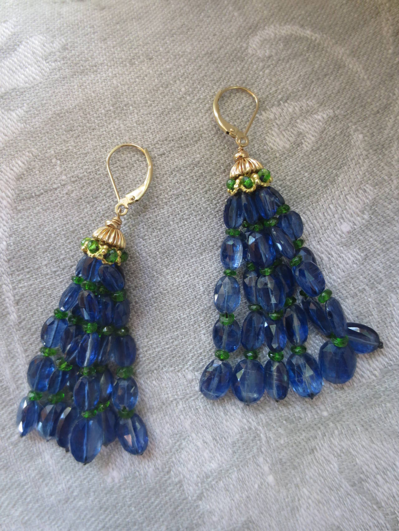 Oval cut deep blue kyanite and small vibrant green tsavorite beads elegantly drape in these tassel earrings. 14 karat gold cups adorn the top of these tassels, and are accented with tsavorite stones. These earrings are rich in color, and hang