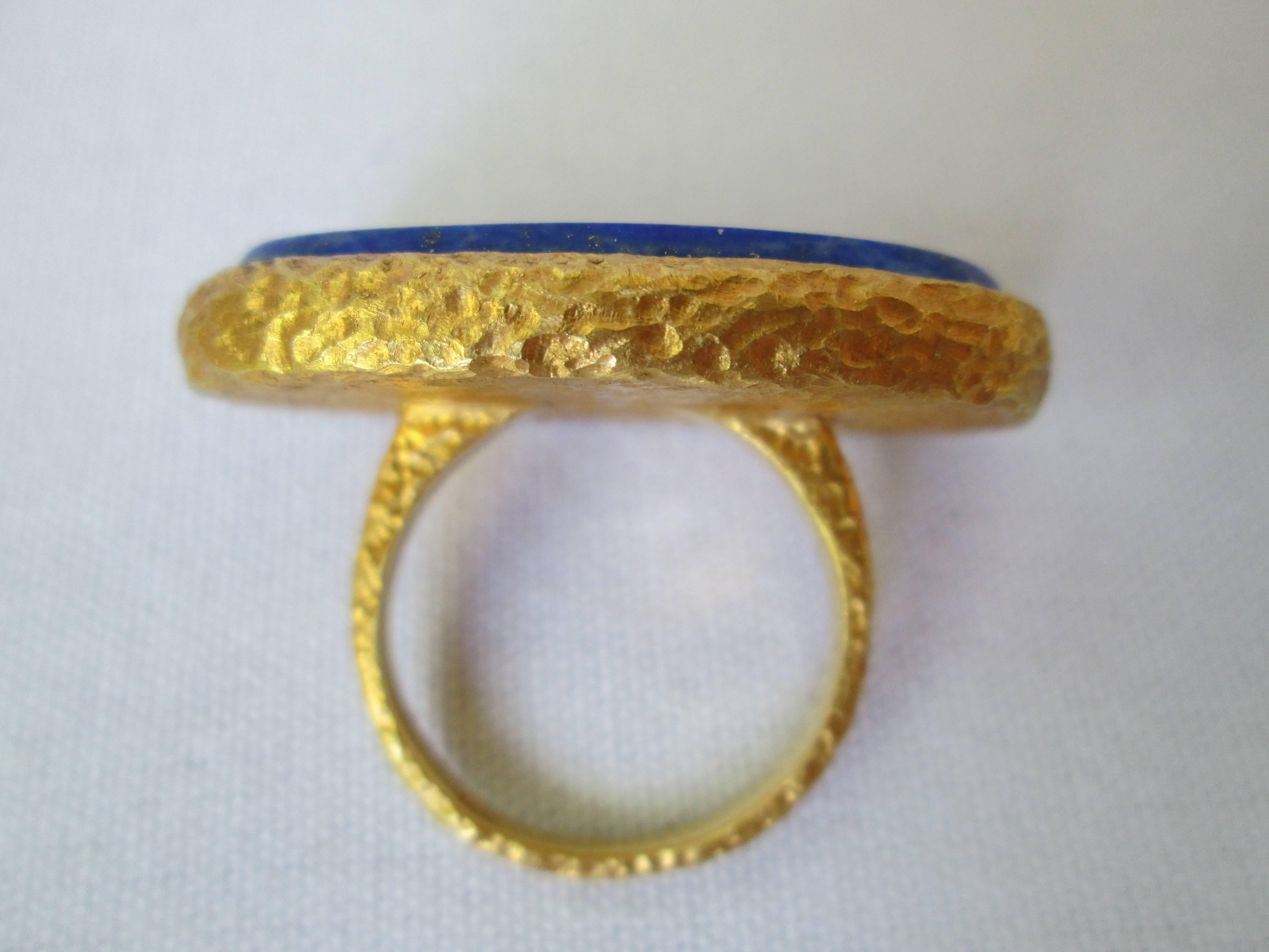 This original and stylish ring evokes the timelessness of antiquity. A large and smooth Lapis Lazuli oval stone is embedded in a hand hammered 18K Yellow Gold ring. The ring is sized 6.5. The Lapis Lazuli oval stone measures 30mm long and 16mm wide.