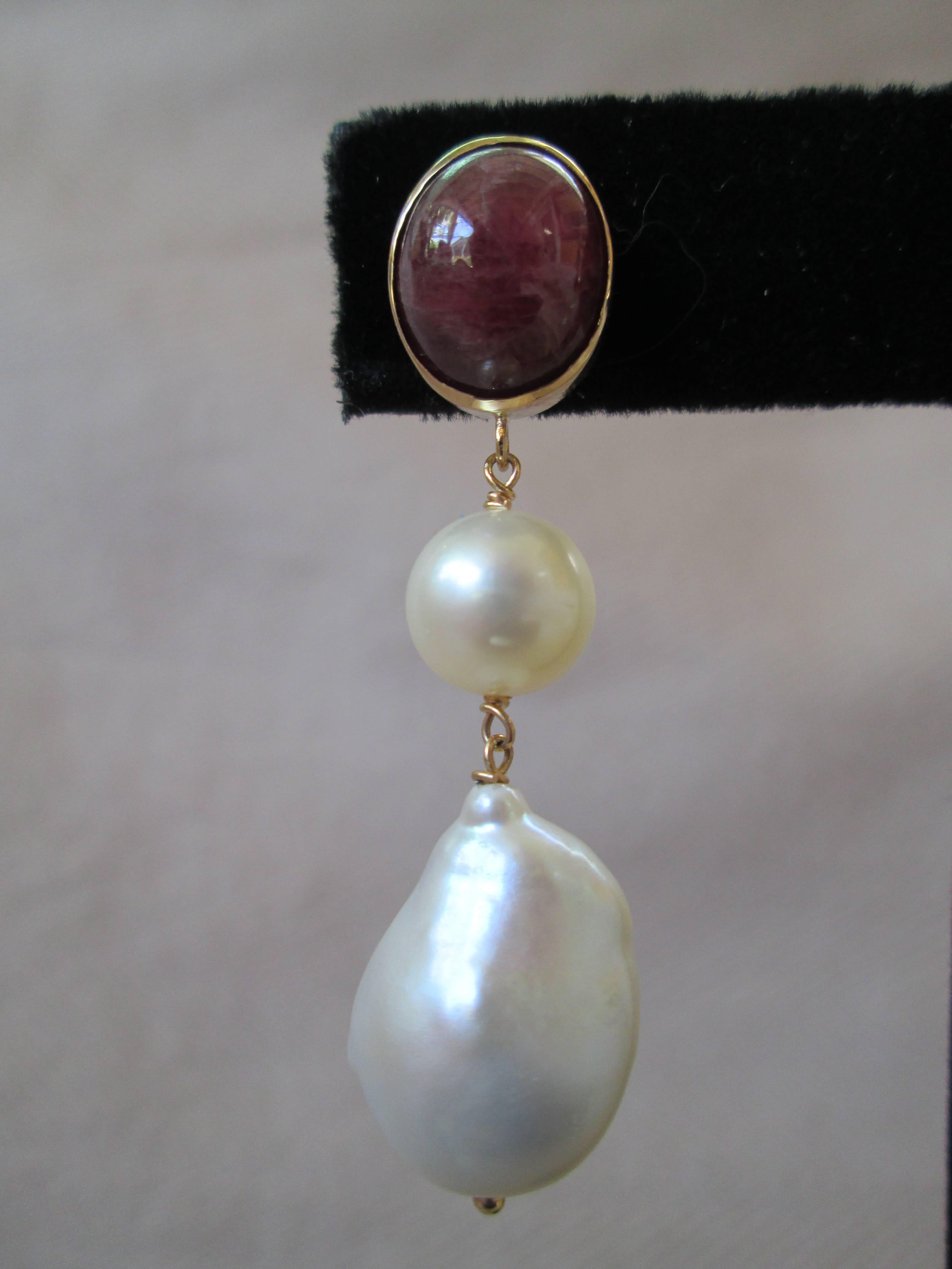 A large Ruby cabochon stone (11mm x 9mm) sits atop a round, 8.5mm pearl and a large teardrop, Baroque pearl. The trio is suspened by 14k yellow gold findings. The ruby cabochon sits in a 14k yellow gold setting. Top to bottom measures 1.75