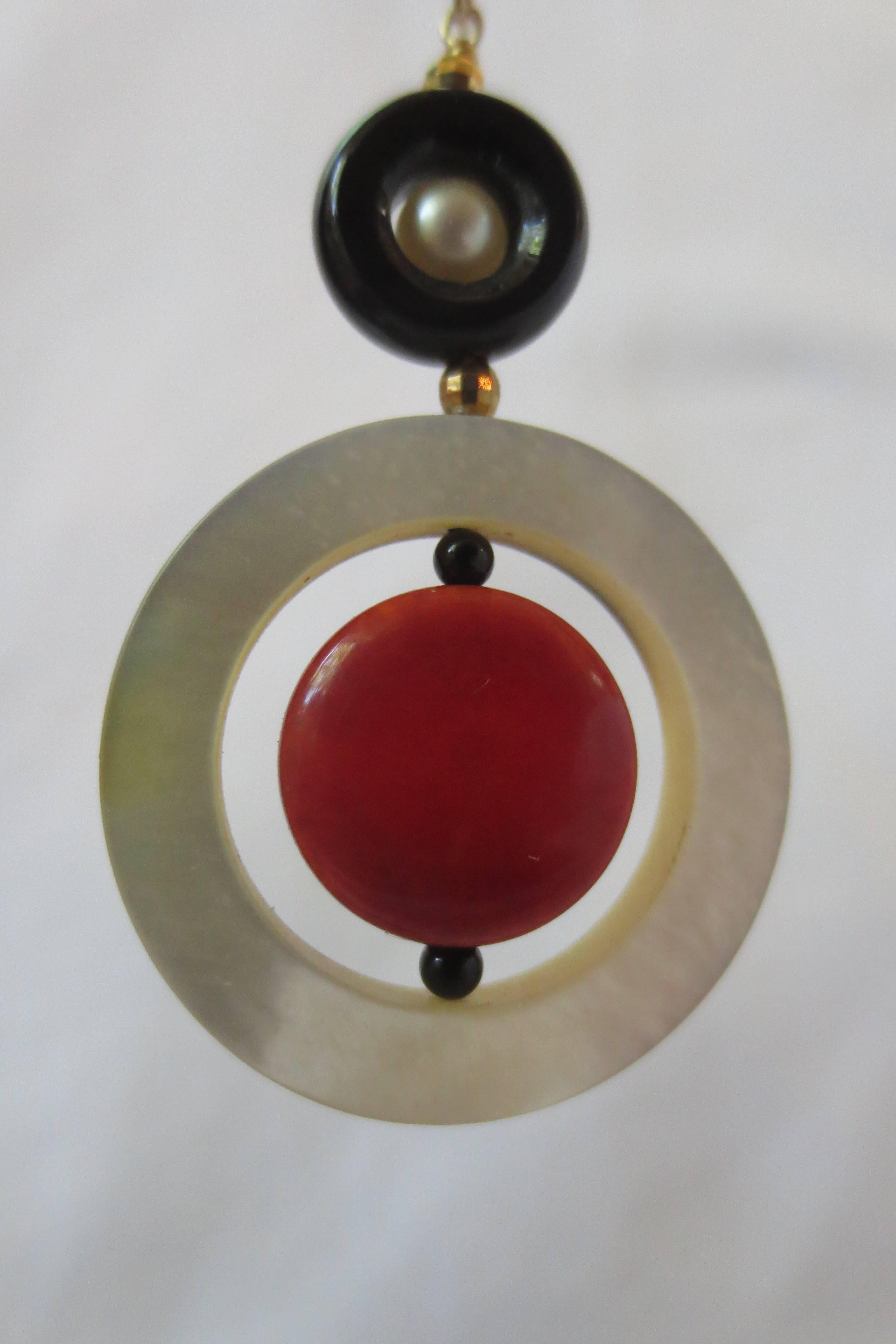 These playful yet interesting earrings are sure to strike a conversation. On top, a round 3 mm pearl is nested in an onyx torus. Below, a round and flat coral bead, is suspended in a large mother-of-pearl ring. The coral bead can spin freely.
