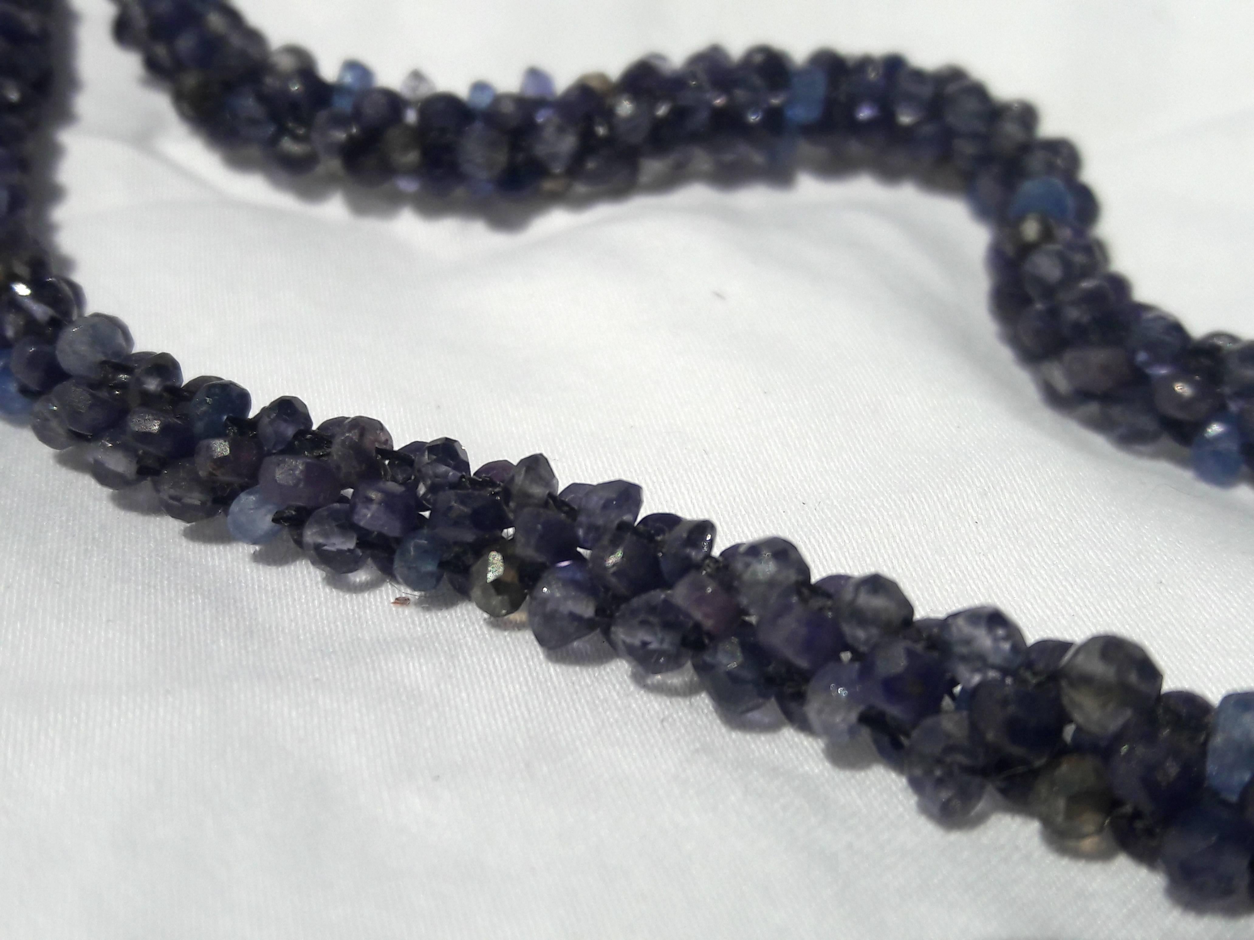 Woven into a tight rope-like strand, faceted Iolite and rough-cut Sapphire beads meet in a contrasting pattern of jagged textures. Secured with two 14 k White Gold clasps that open and connect to a Rhodium-plated silver cross pendant. The Cross