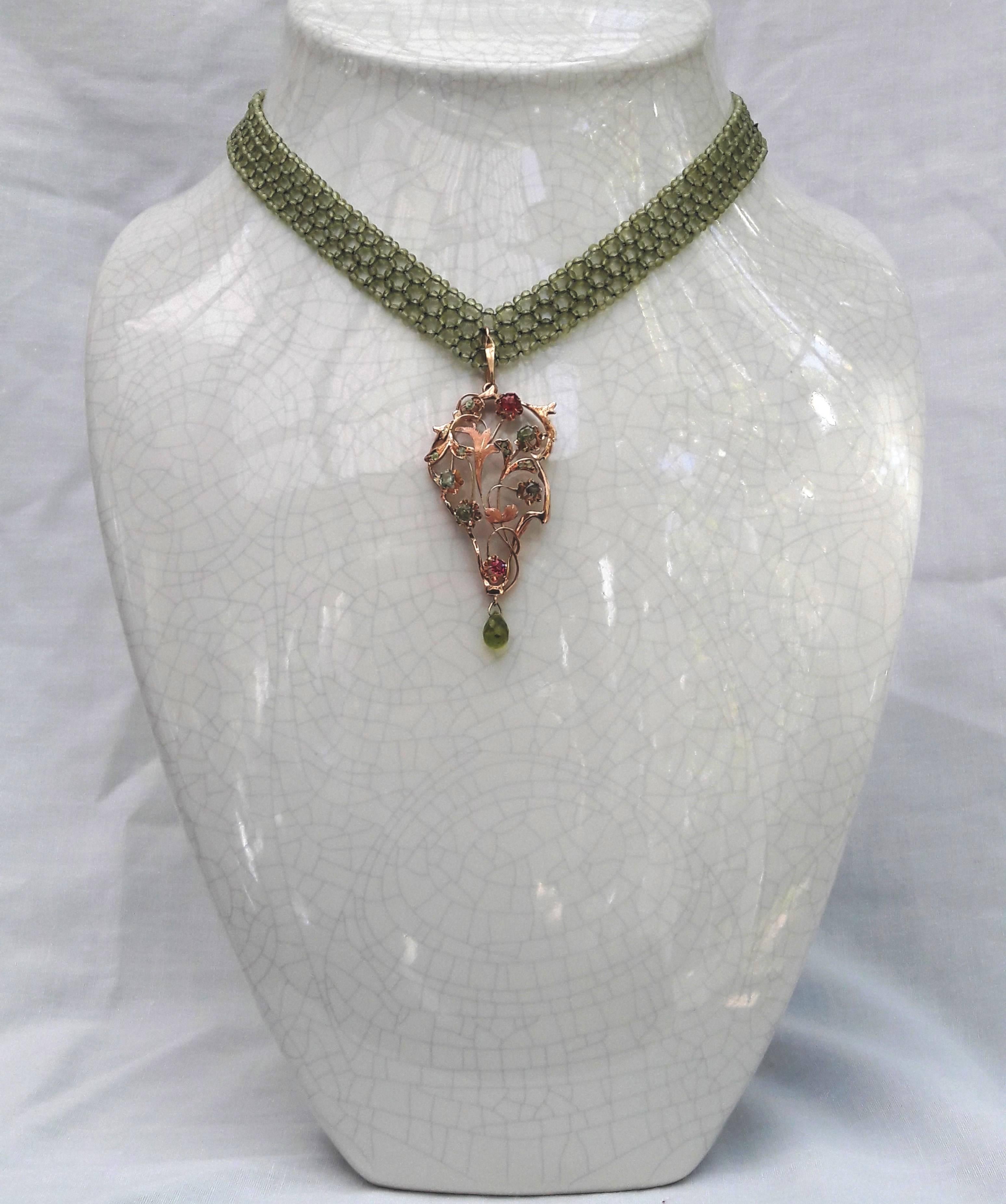 The necklace is composed of fine and faceted 1 mm Peridot beads, and woven into a flat, v-shape ribbon. 

Suspended in the center is a vintage 14 k yellow gold pendant, exquisitely detailed in a floral motif and glistening with faceted Ruby and