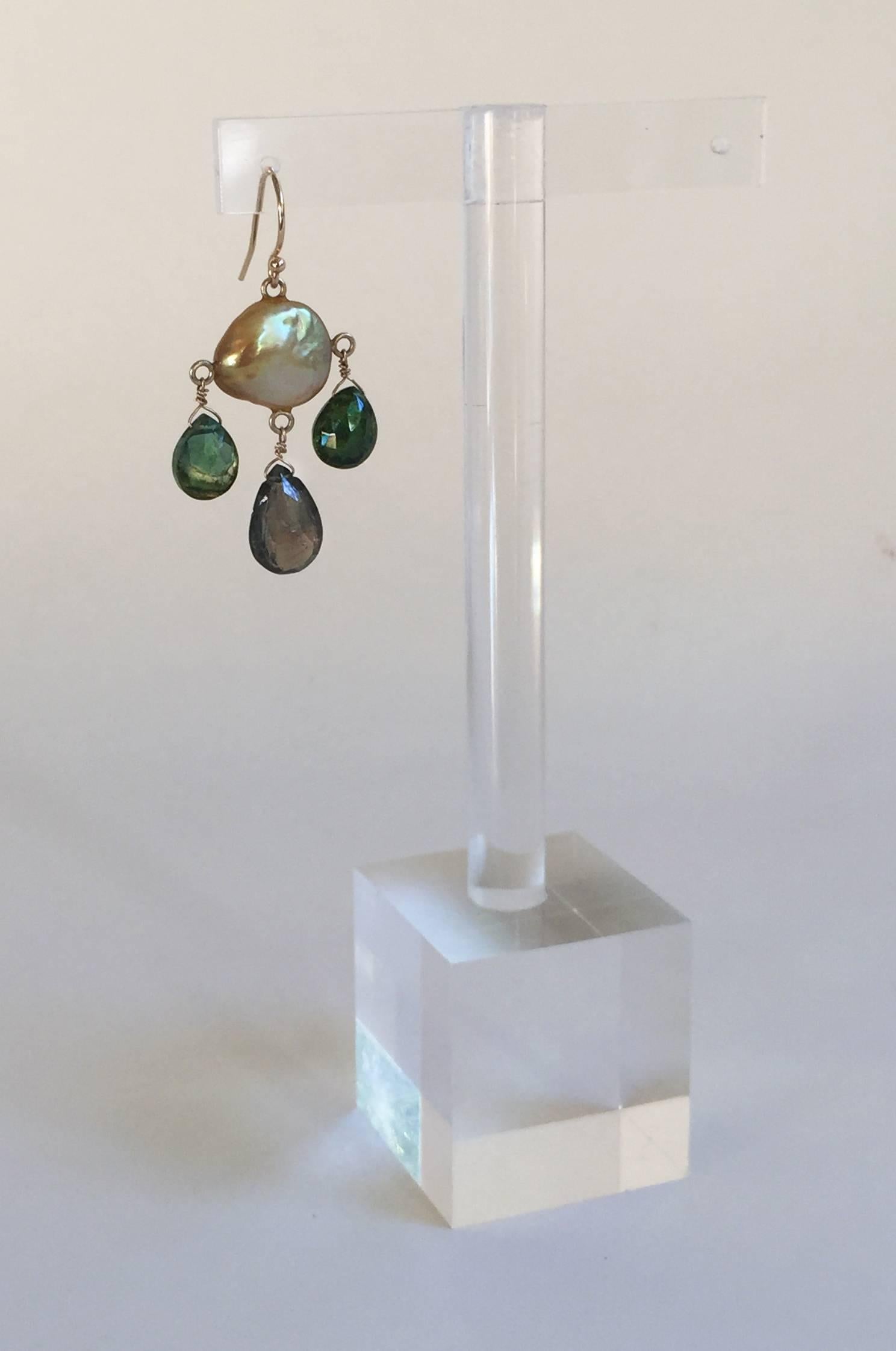 The golden hue of the coin pearls is accented by dark forest green tourmaline briolettes. The earrings are completed with 14k yellow gold hook and wiring, perfect for the fall season. They hang at 1.75 inches to highlight the face and accentuate the
