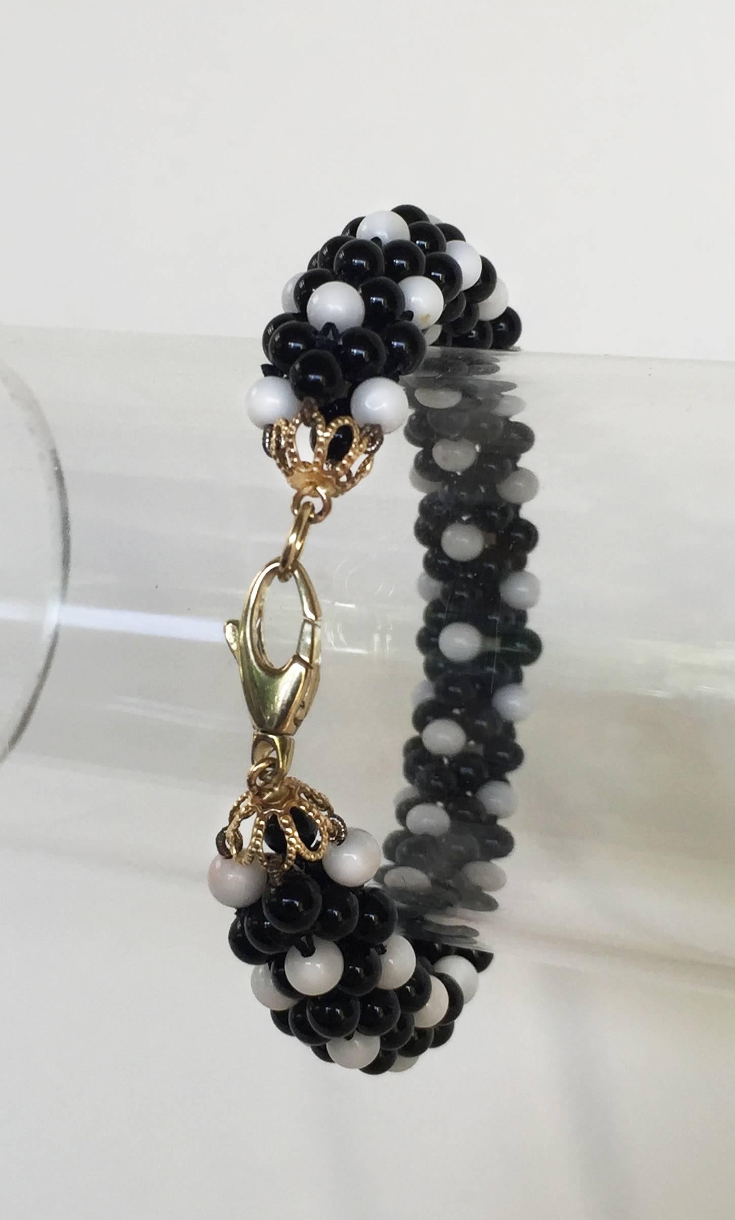 This intricately woven rope bracelet is composed of white coral and black onyx beads with a 14k yellow gold clasp. The black and white checkered effect is reminiscent of  1960s Mod fashion. At 7.5 inches long and 1 inch thick, it fits perfectly on