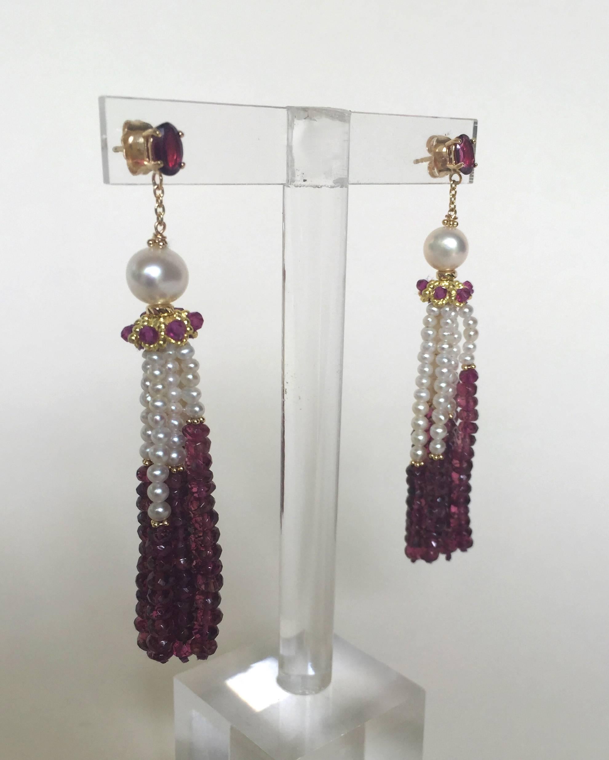 The graduated pearl and faceted garnet strands of these tassel earrings are highlighted by 14k yellow gold beads. A 14k gold cup with shimmering faceted garnet beads running through holds the earring together. On top is an elegant round white pearl