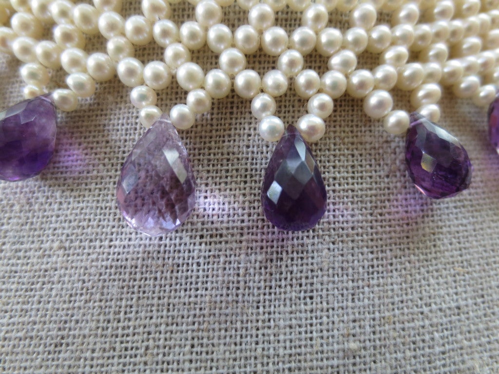 A handwoven necklace made of 2.5 mm cultured pearls and graduated, faceted, teardrop amethyst briolettes. Necklace measures 16 inches in length and is approximately 1.25 inches in width. Made with finely detailed 14 karats yellow gold clasp.