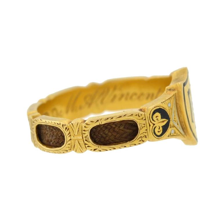 This rare English mourning ring from the Victorian (ca1879) era is quite an unusual piece! Crafted in 18kt gold, the ring is richly detailed, and serves as a fine example of the mourning jewelry tradition. Black and white enameled accents decorate