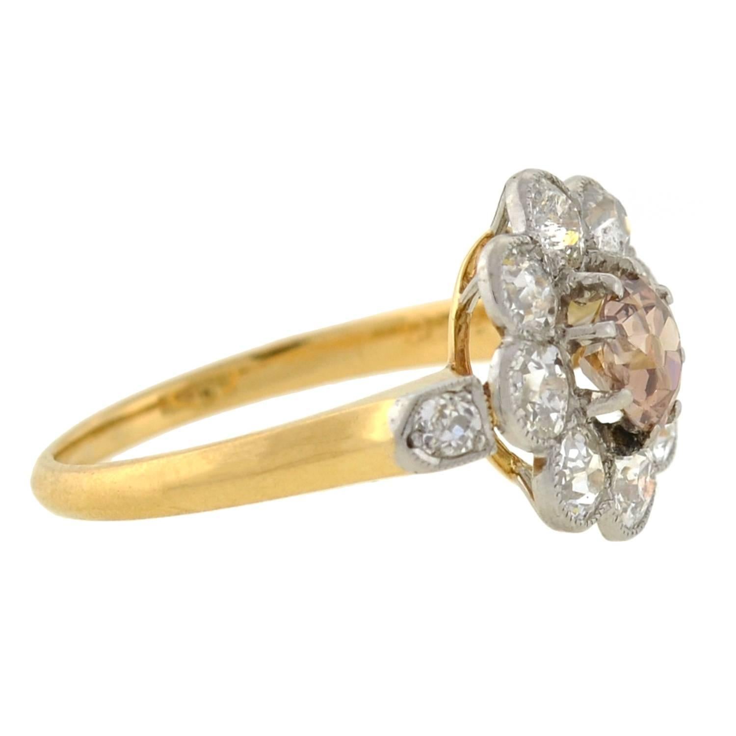 An exquisite diamond cluster ring from the Edwardian era (ca1910)! This gorgeous ring is crafted in 18kt gold topped in platinum, and has an elegant flower-inspired design. A stunning old Mine Cut champagne diamond is prong set at the center,