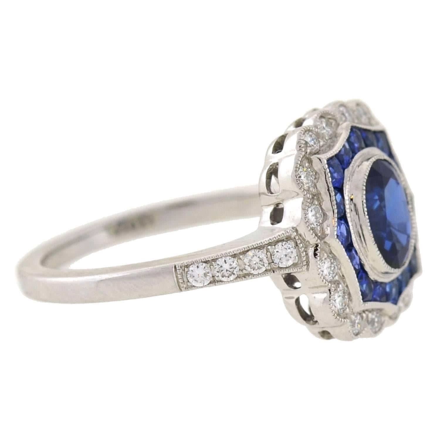 This spectacular sapphire and diamond ring is an estate piece inspired by the Art Deco era! Crafted in 18kt white gold, the ring frames a deep blue sapphire stone at the center of a decorative mounting. The oval cut sapphire weighs approximately