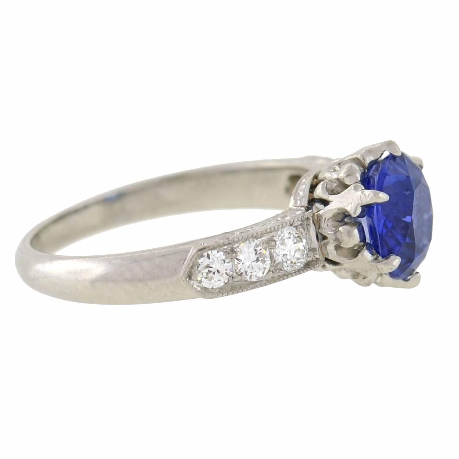 A stunning Art Deco style sapphire engagement ring! Made of platinum, this fabulous piece features an exquisite 1.50ct sapphire at the center. The sapphire rests within a crown-like prong setting and displays a magnificent rich blue shade. Lining