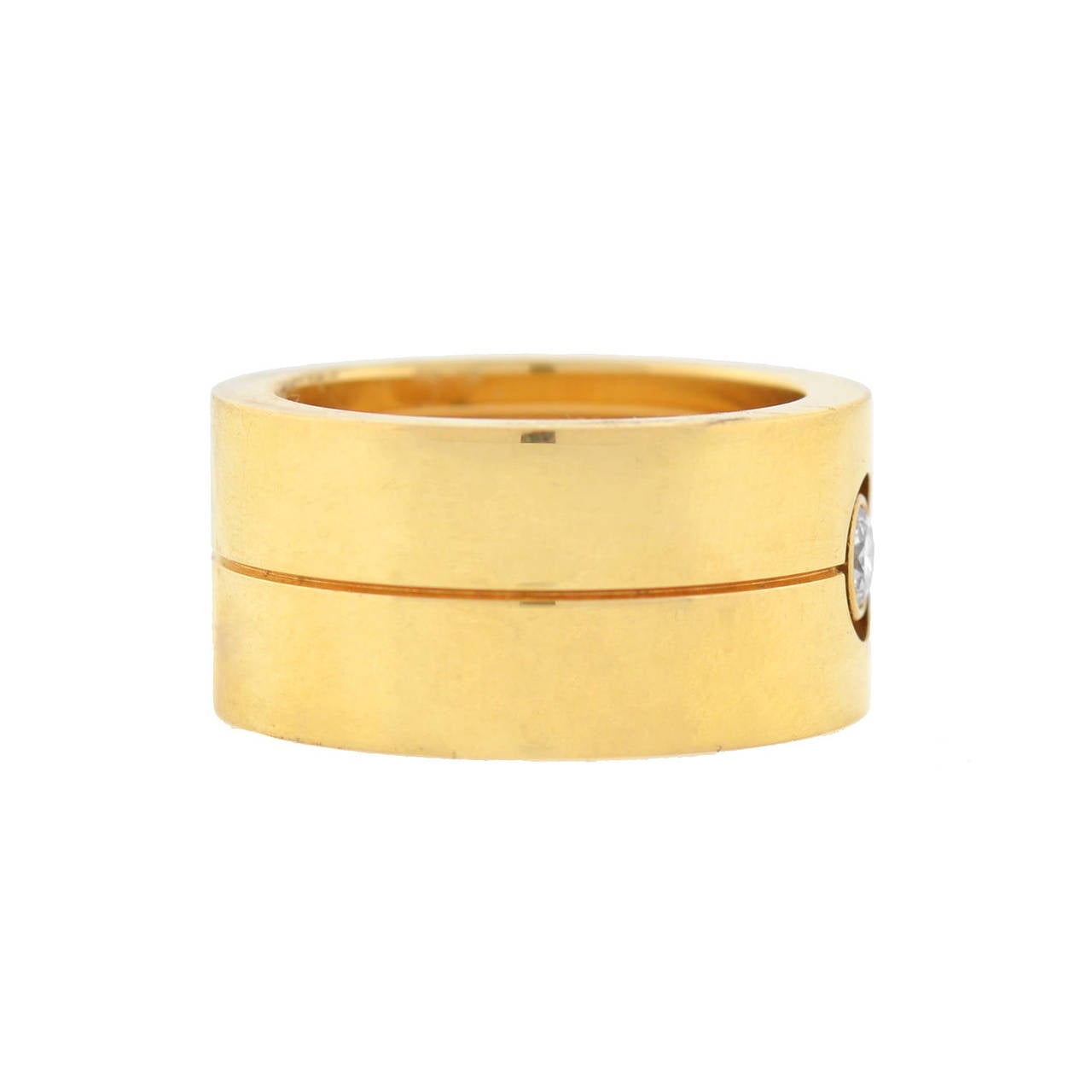 This fabulous ring is a signed piece by Cartier! Made of vibrant 18kt yellow gold, the heavy, wide ring has a striking design and is substantial in size. A sparkling bezel set diamond rests in the center, set within a circular airline. An engraved