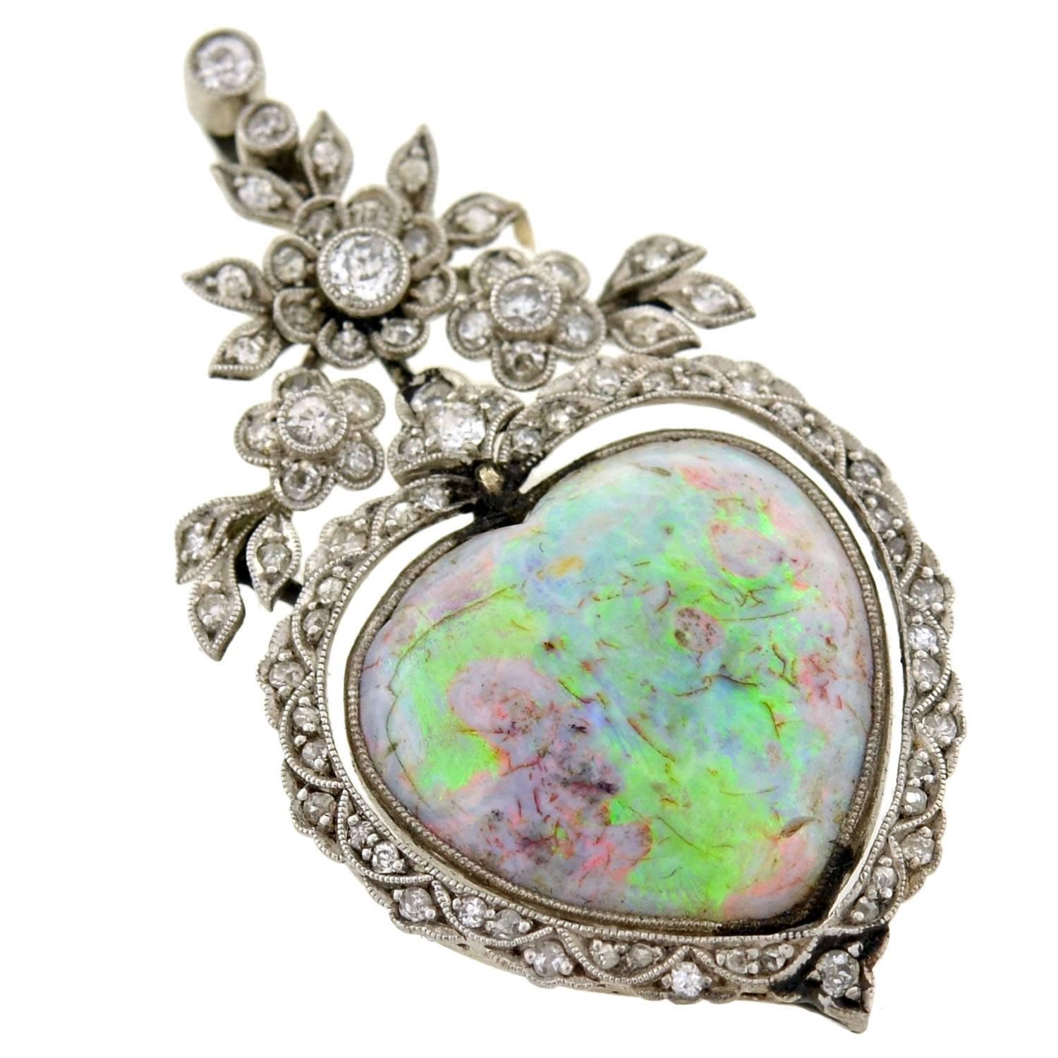 A stunning opal pendant from the Edwardian (1910) era! This delicate piece depicts a large, heart shaped opal which is surrounded by sparkling diamonds. The opal, which is vibrant in color with hues of green, pink, purple, blue and yellow, is bezel