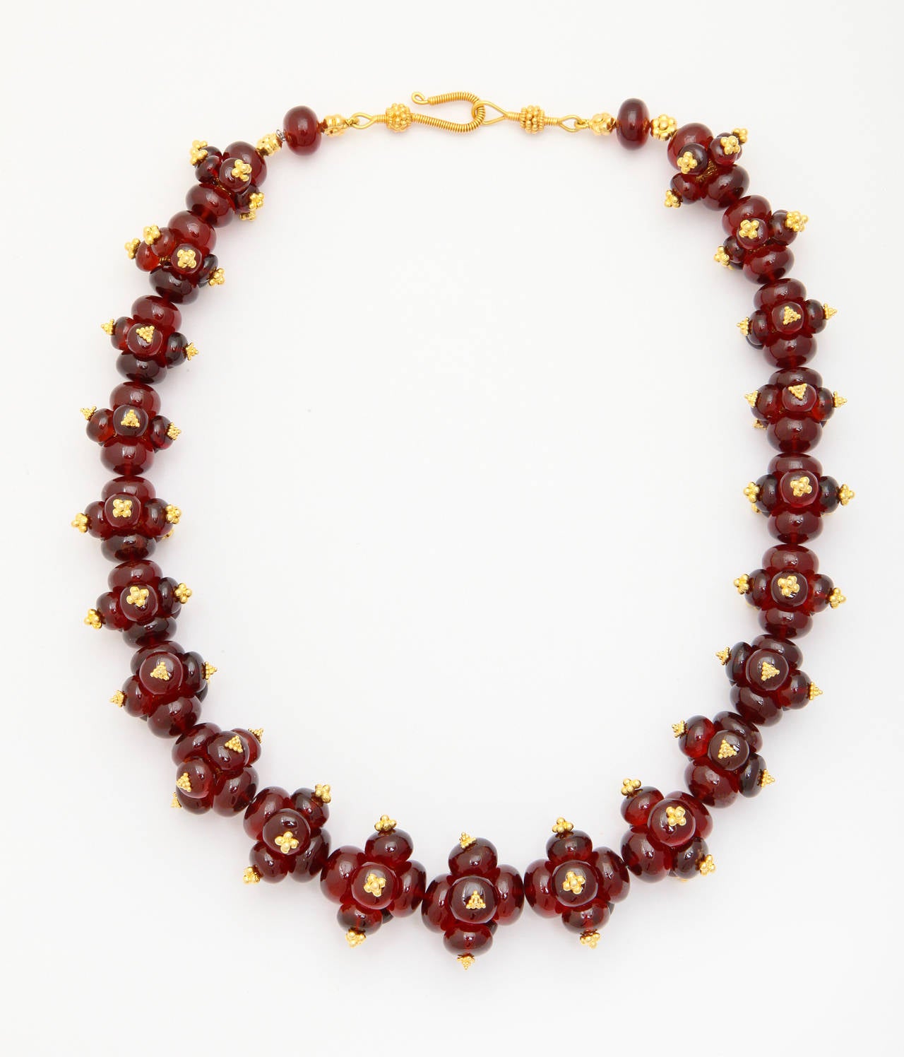 A necklace composed of garnet beads, 18kt yellow gold granulated flower beads and an 18kt yellow gold clasp.