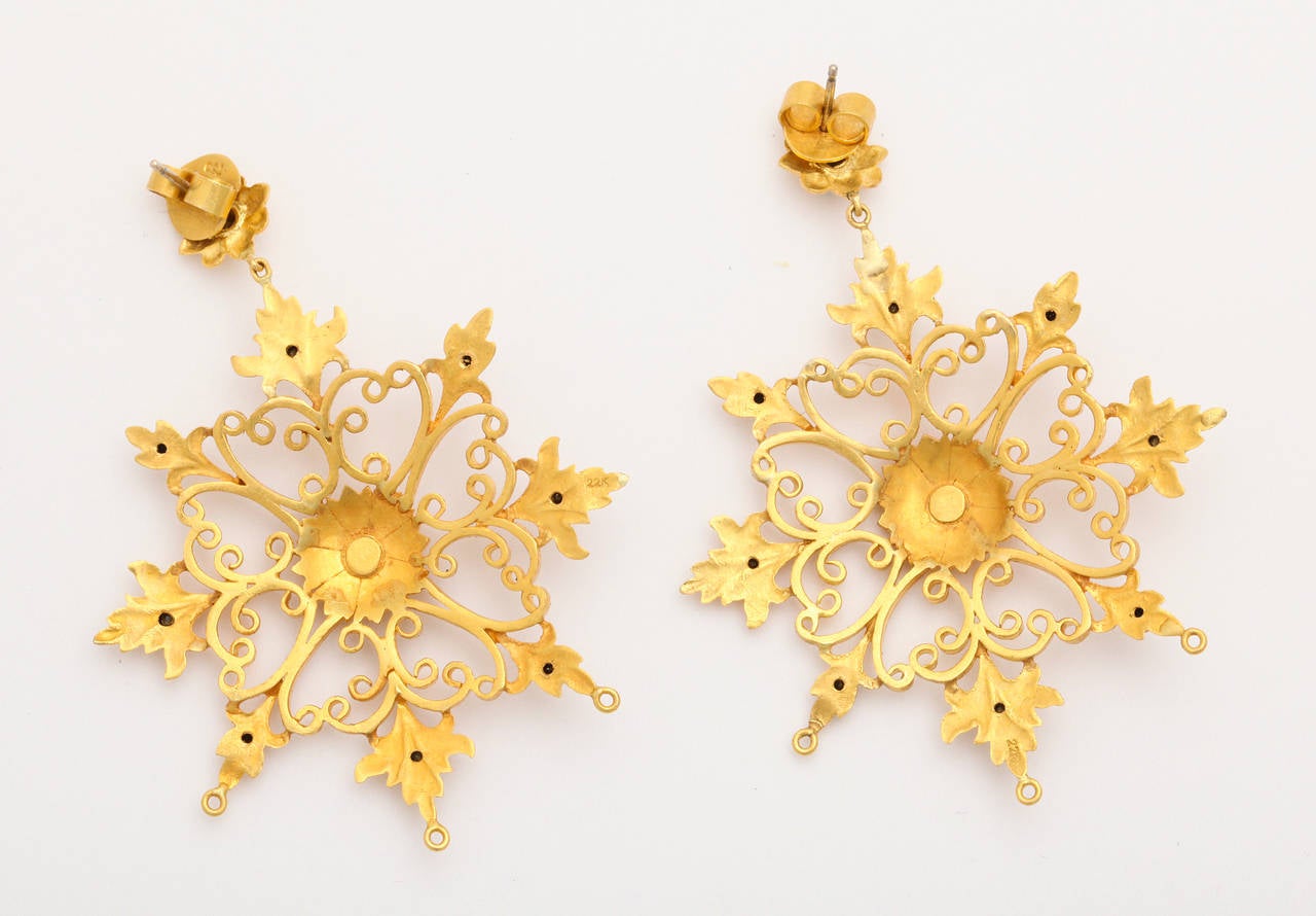 A pair of earrings composed of 18kt yellow gold snowflakes. The snowflakes are set with 1.46cts of black diamonds and .17ct of round brilliant cut diamonds. The snowflakes are suspended from 18kt yellow gold flower studs which are set with .16ct of