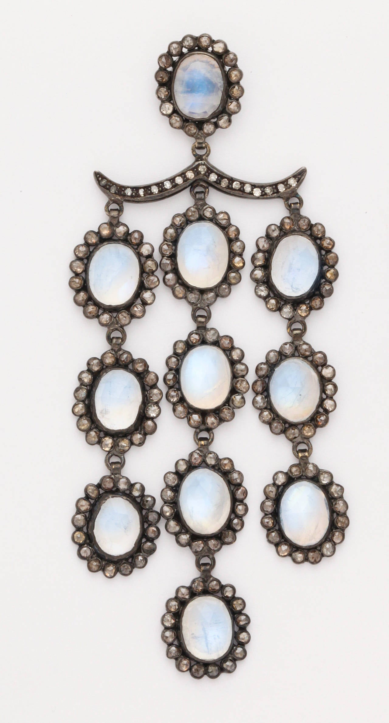 A pair of moonstone, rose cut diamond and rhodium plated sterling silver earrings.The earrings are composed of cascading moonstone and diamond pendants suspended from diamond set bars. The diamond bars are suspended from moonstone and diamond
