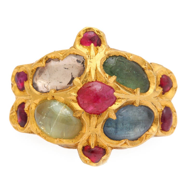 An 18kt yellow gold contemporary mogul ring. The ring is set with a cabochon sapphire. a cabochon emerald, a cabochon cats eye chrysoberyl, a polki diamond and cabochon rubies. There are decorative shields on either side of the ring. Size
