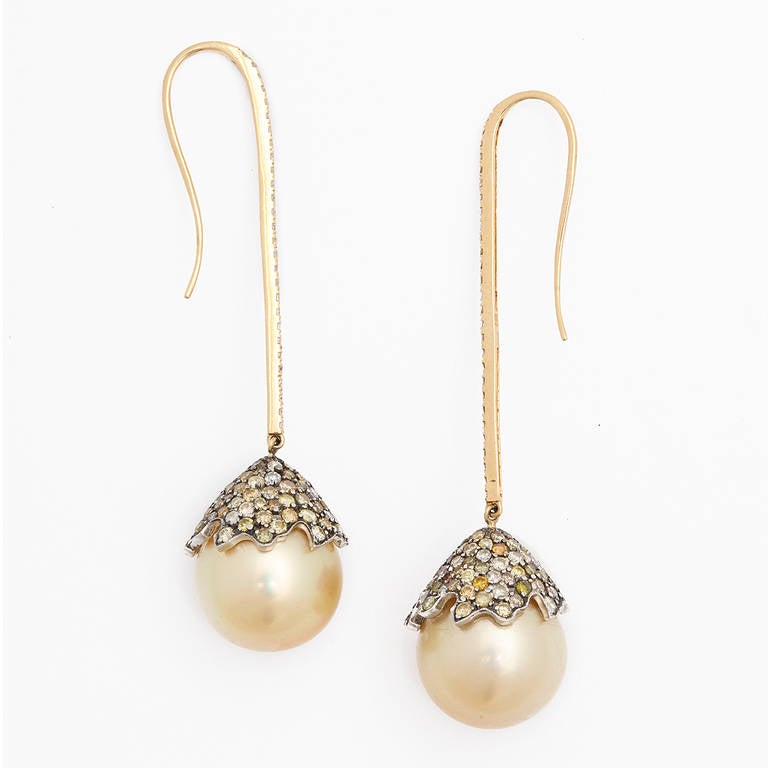 A pair of golden South Sea pearl drop earrings. The pearls have rhodium plated 18kt gold starfish caps that are set with multi colored round brilliant cut diamonds. The pearls are suspended from 18kt yellow gold sticks which have been set with