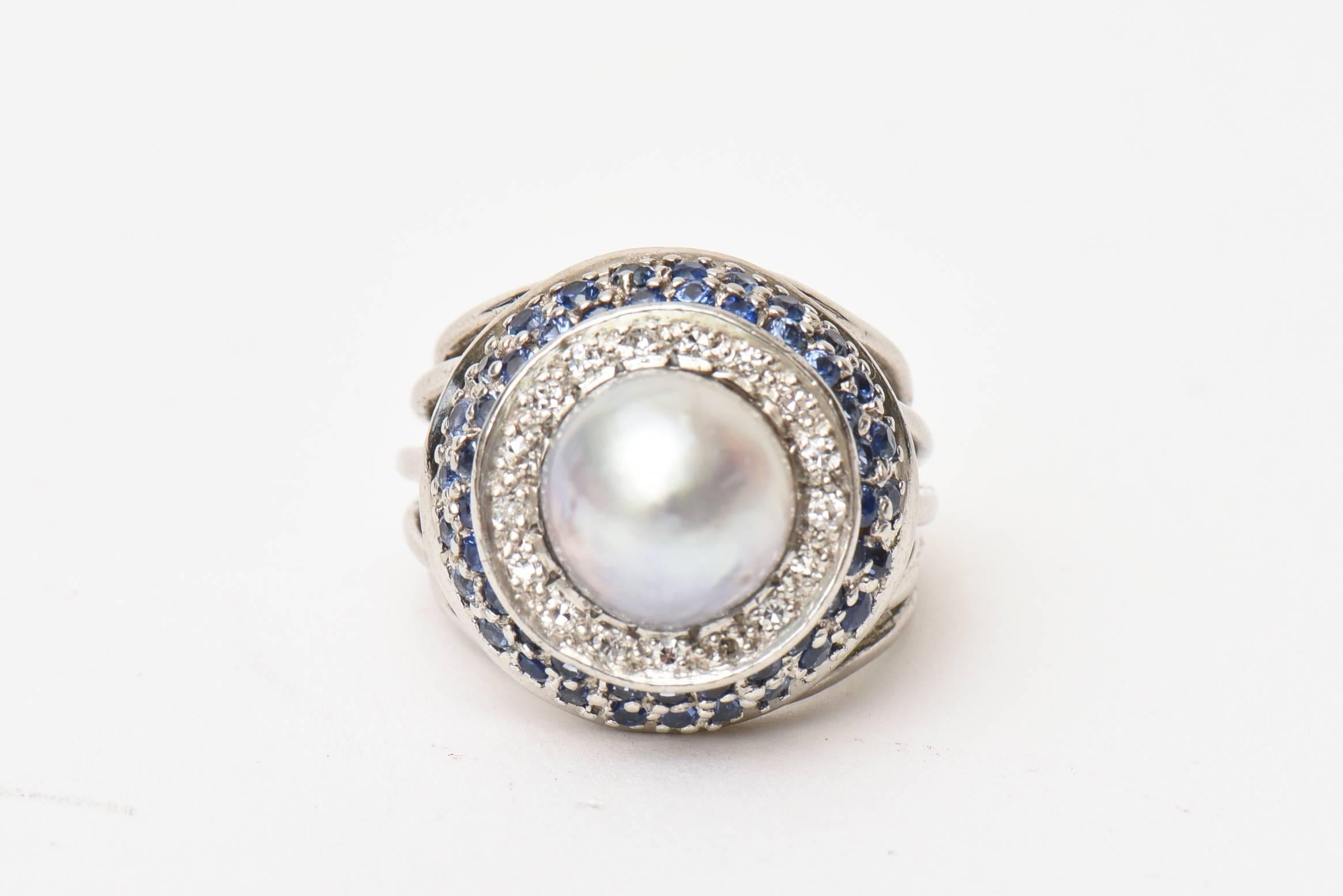 This classic and vintage dome cocktail ring features elements of an off gray cultured round pearl, sixteen round cut diamonds and and fifty round mixed sapphires. It is timeless and elegant. Great for day or evening. There are 5 bands of 14K white