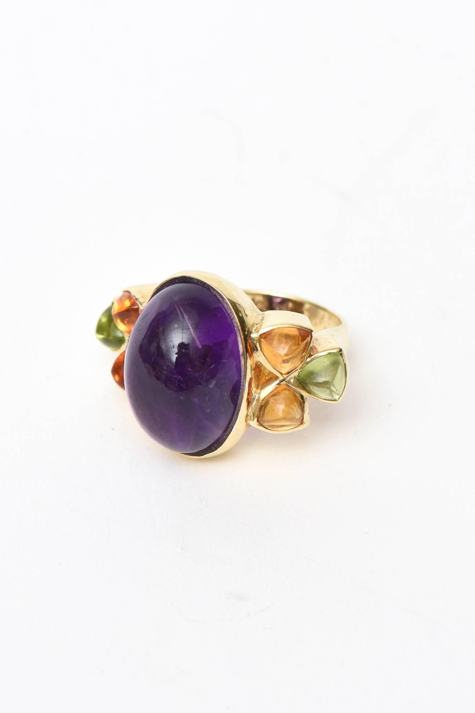 Este colorido y encantador anillo de cóctel o anillo vintage puede llevarse tanto de día como de noche. Tiene una gran piedra amatista en el centro y está rodeada a ambos lados por citrino y peridoto. Se trata de una amatista oval tallada en cabujón