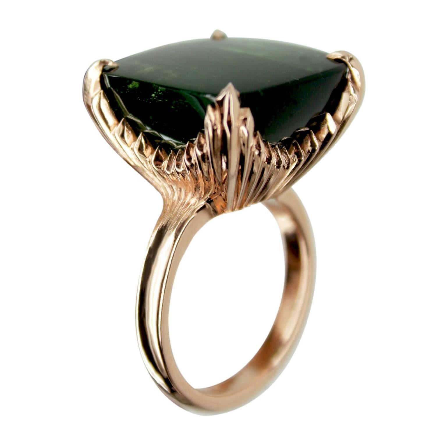 A stunning one-off 23 ct buff top cushion cut deep green tourmaline stone, set into a four claw 9ct rose gold ring.

The detail carries on underneath to create a raised mount of grooves and filed angles. This really catches the light as you move the