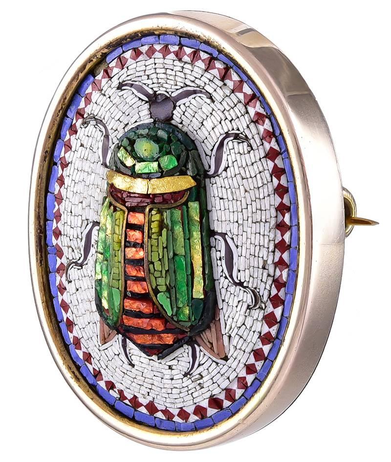 The colourful rounded Scarab decorated in Green, Gold, Orange and Black on a white mosaic background with a red diamond pattern and blue line borders.
The reverse plain with a good pin and catch and the unmarked Gold tests for 18K. A fine example of