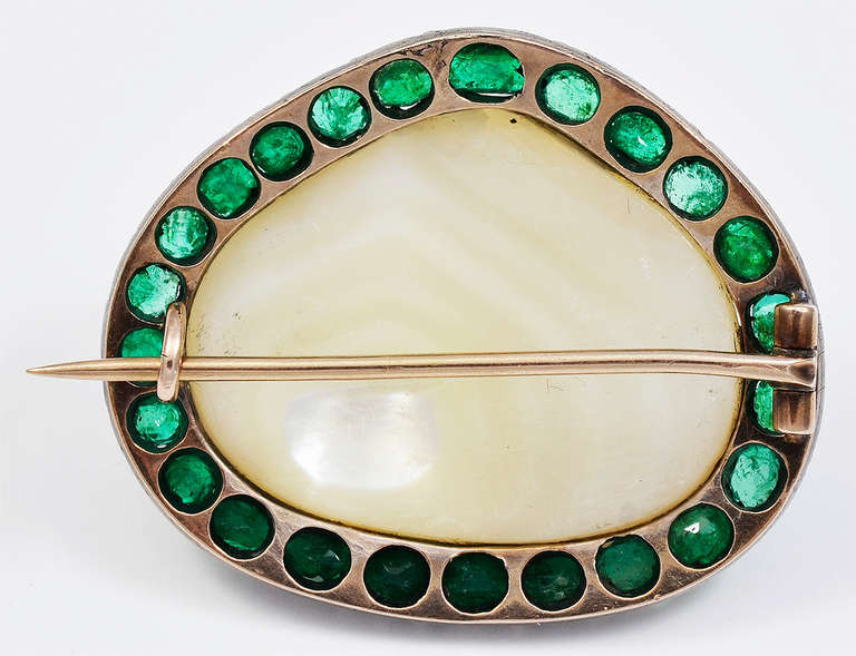 The large Pearl with a good luster, the mount Silver on Gold with a surround of twenty four Emeralds, all in open backed settings, two having small chips which are visible with a hand lens, other than that, the Brooch is in good condition.