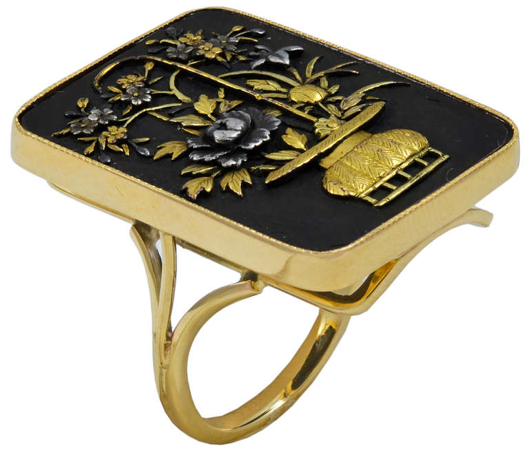 The rectangular top with a Gold Japanese urn containing a profusion of Gold and Silver Flowers which almost fill the whole surface. The slender Gold Ring mount is circa 1930's and the Shakudo top is circa 1890.

A most attractive Ring which can be