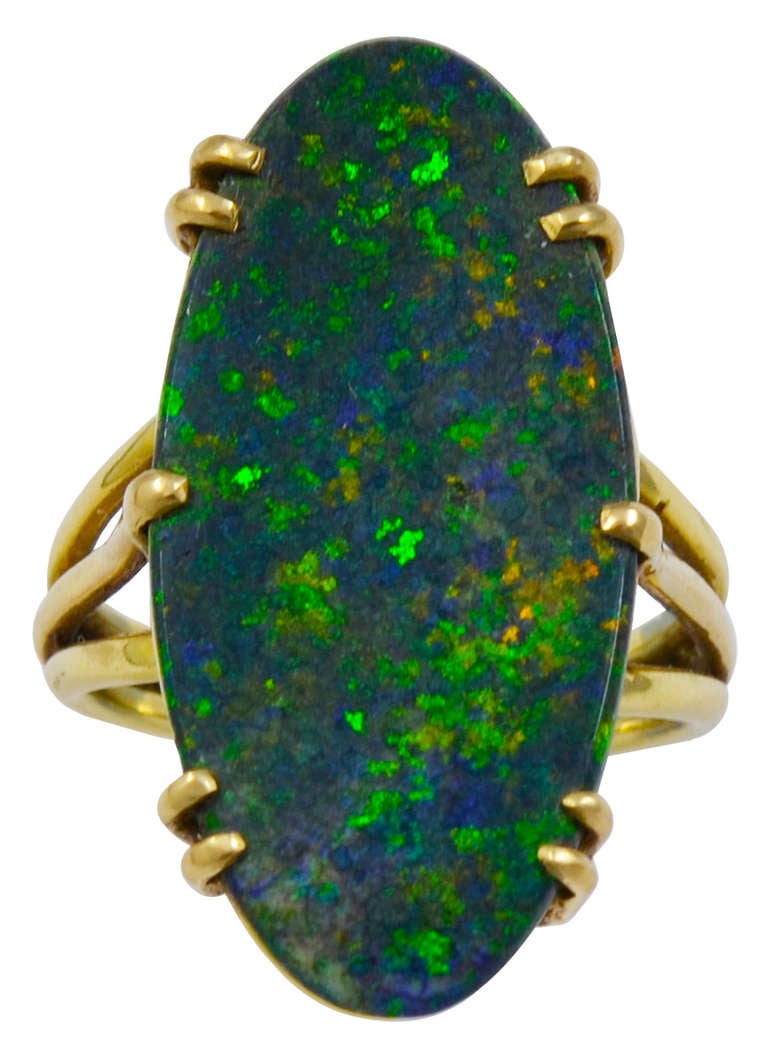 The very long and thick oval piece of mysterious Black Opal is held by four double and two single prongs and shows the colors Green, Blue and Orange whilst being worn and in movement. The reverse of the stone is visible and is also a good color. The
