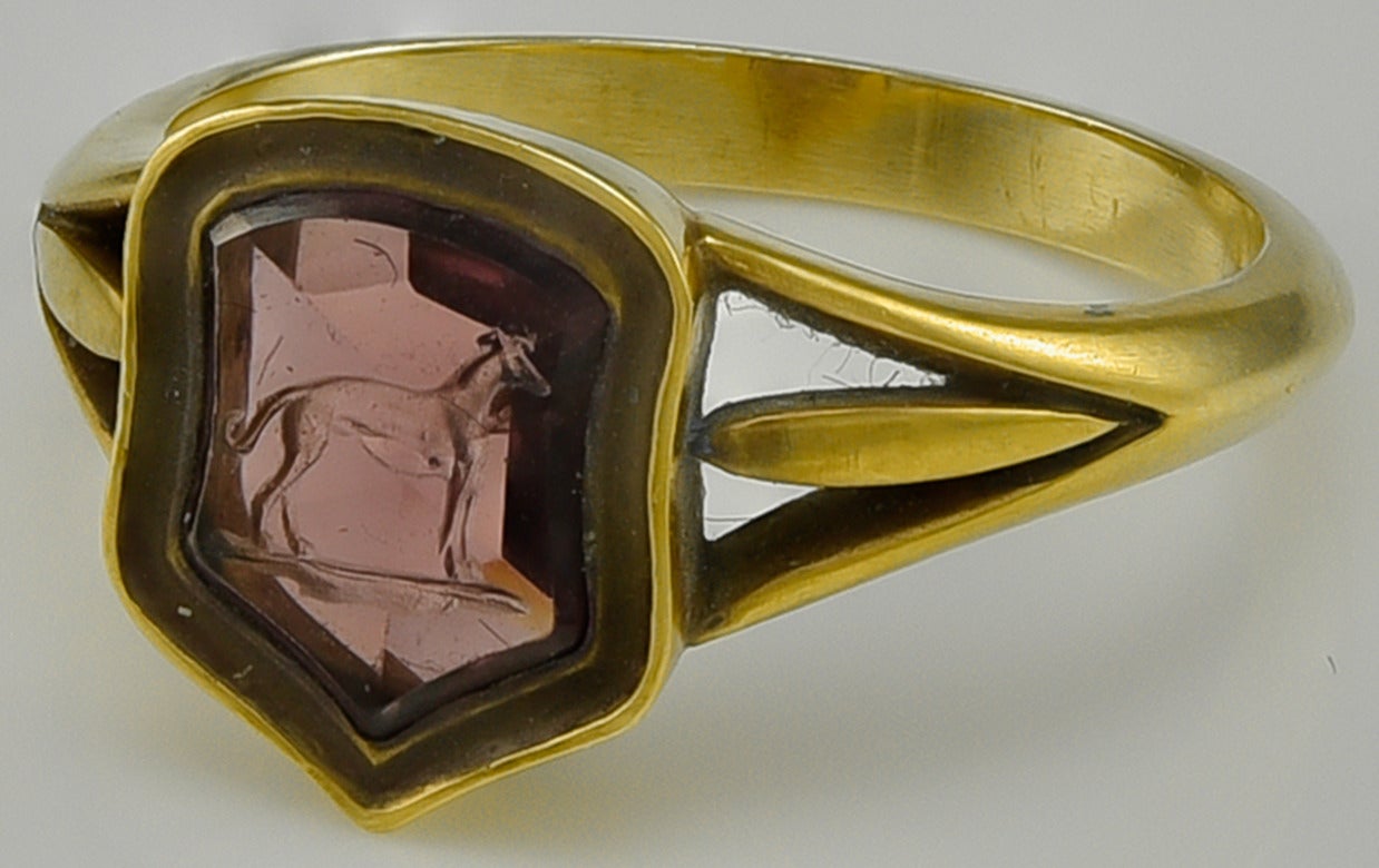 The slightly shield shaped red/mauve Garnet is engraved with the image of a Greyhound standing on a ground line. This is part of an Heraldic Crest and would have been used for sealing minor documents and personal letters.
The Gem is set in an