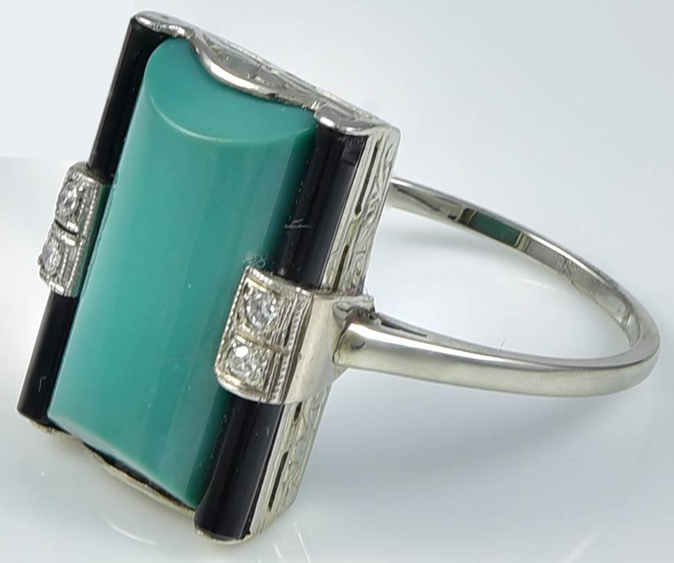 With a central loaf shaped Green Turquoise and on either side, a pair of old mine Diamonds set centrally on rods of Black Onyx. The Ring has an attractively engraved gallery to a slender shank stamped with a makers mark and testing for 18k White