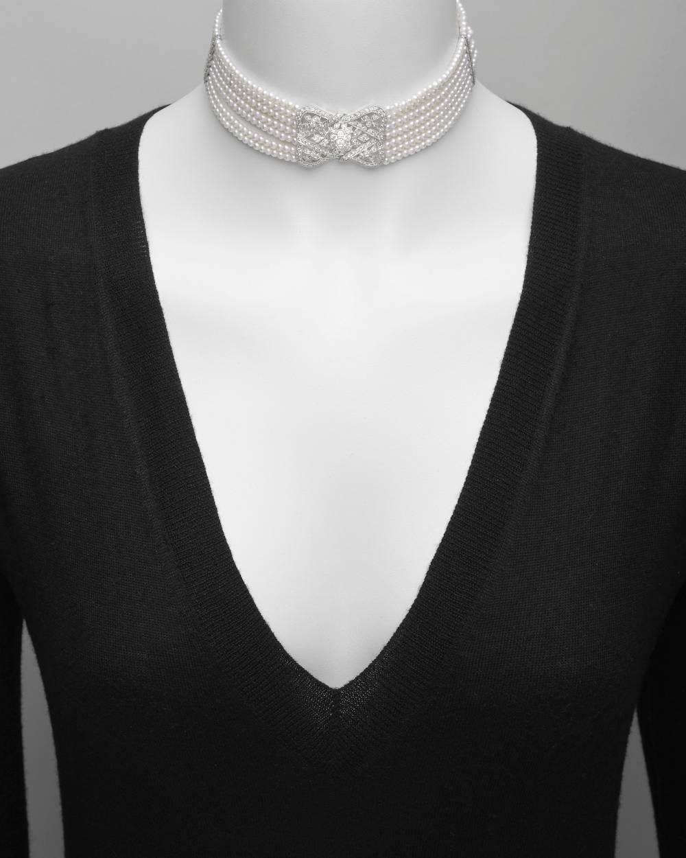 Edwardian-style 7-strand pearl choker necklace, centering a pierced diamond-set panel of ribbon and floral motifs, with two diamond spacer bars, the necklace secured by a dagger-style clasp with pavé-set diamond teardrop pendant, mounted in 18k