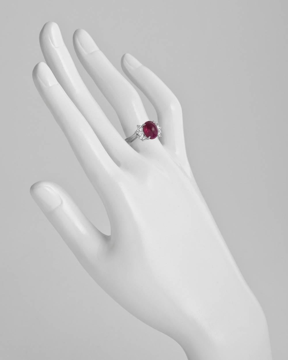 Cluster ring, centering an oval-shaped cabochon-cut ruby weighing approximately 3.12 carats flanked by a cluster of round brilliant-cut, pear-shaped and marquise-shaped diamonds at either shoulder, the diamonds altogether weighing approximately 0.54