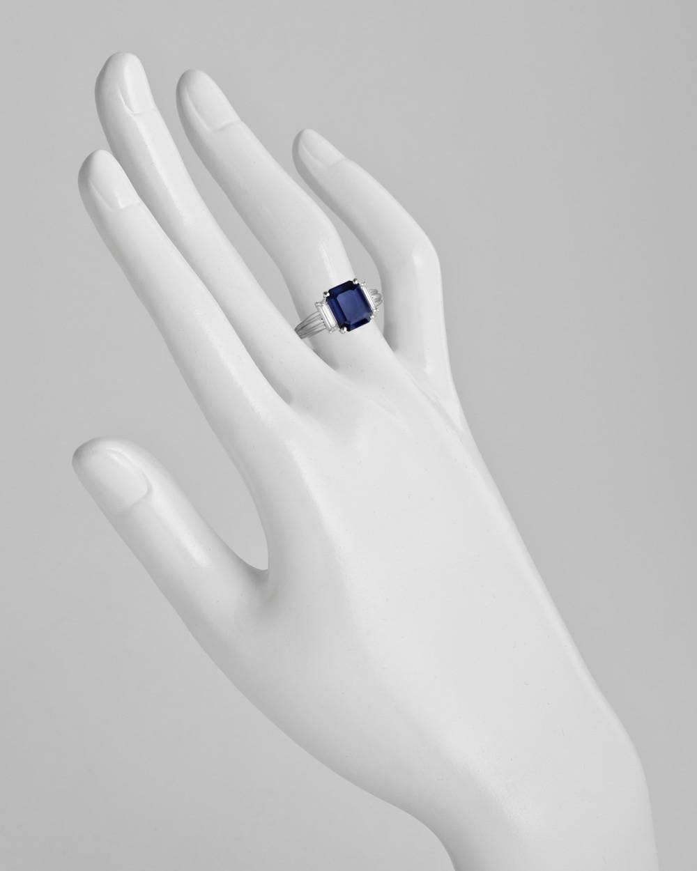 Dress ring, centering an emerald-cut sapphire weighing approximately 2.76 carats, flanked by near-colorless baguette-cut diamond shoulders weighing approximately 0.59 total carats, mounted in a fluted platinum setting. Size 5.25 (resizable to most