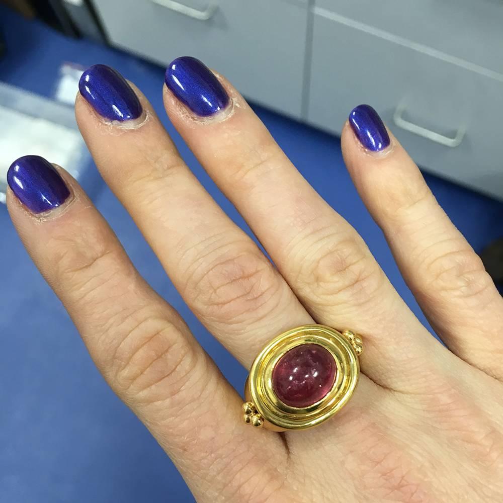 Dress ring in 22k yellow gold, centering a bezel-set oval-shaped cabochon rubellite measuring approximately 12 x 10mm, flanked by triple granulation at either shoulder. Size 8.5 (resizable to most ring sizes).