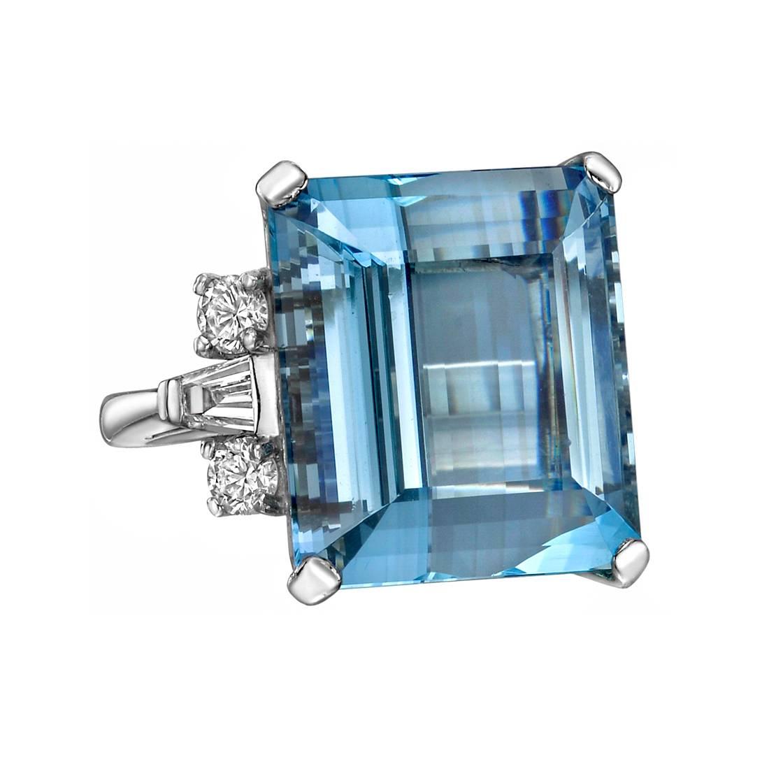 Aquamarine and diamond cocktail ring, centering an emerald cut aquamarine weighing approximately 25.00 carats, with round brilliant cut and tapered baquette cut diamond accented shoulders, in platinum. Four round brilliant cut diamonds weighing