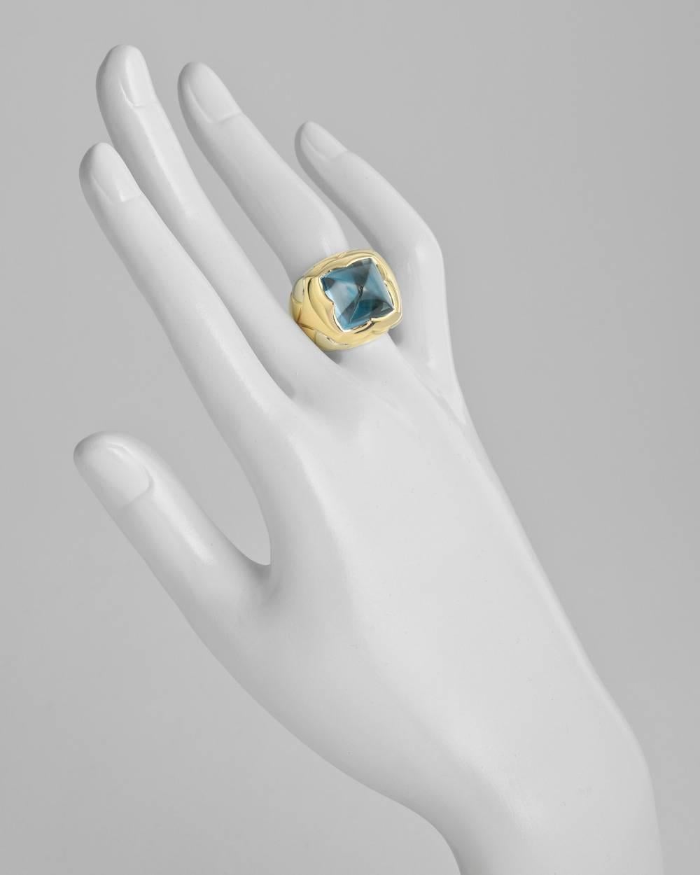 "Piramide" cocktail ring, centering a high-pointed cabochon sugarloaf-cut blue topaz measuring approximately 13.5 x 13.5mm from the top, mounted in polished 18k yellow with white gold elements at shoulders, the ring measuring 20mm across x