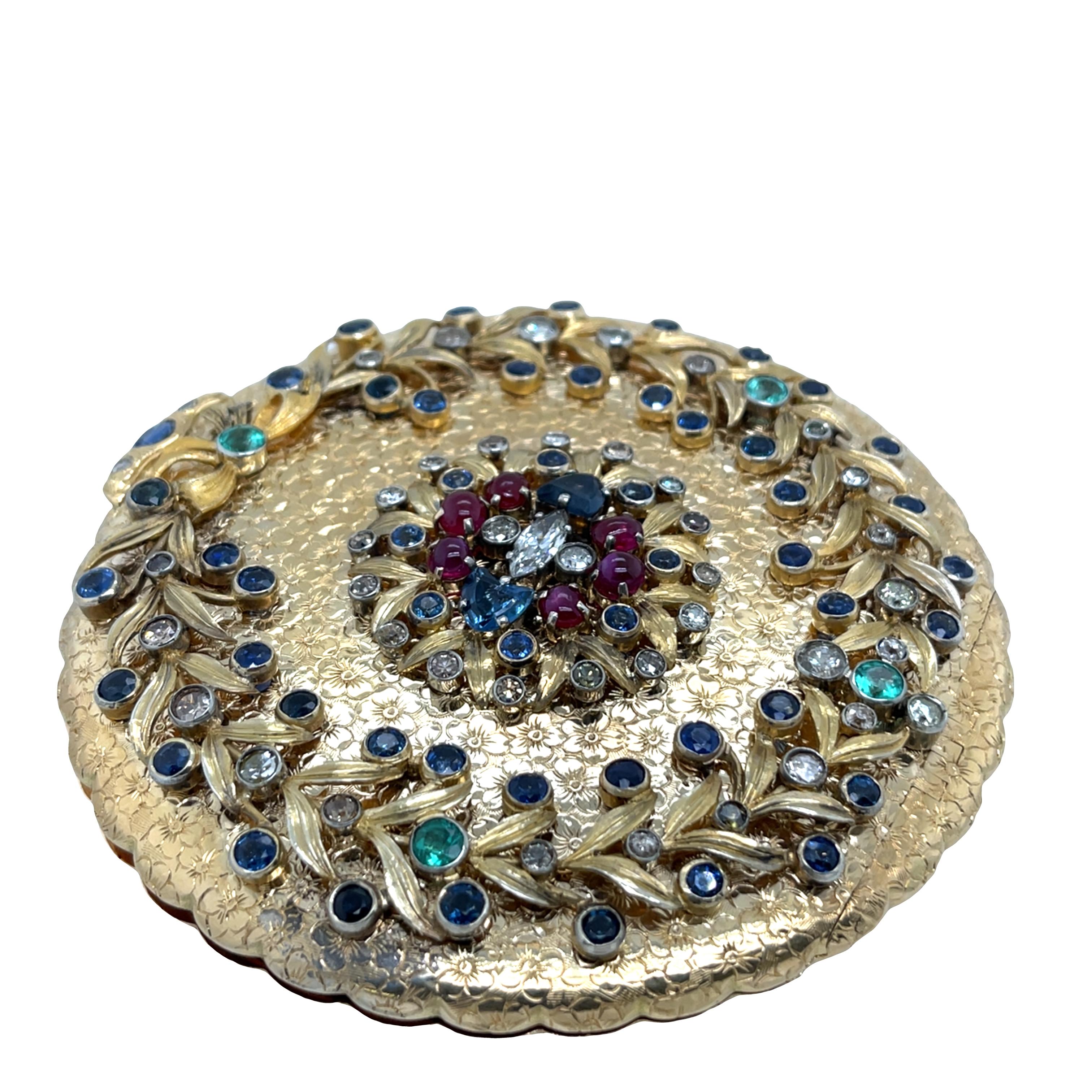 Un poudrier ancien vraiment unique, délicieusement travaillé et orné d'un somptueux éventail de saphirs naturels, d'émeraudes, de rubis et de diamants. Le poudrier est orné d'un délicat motif de fleurs d'oranger gravé à la main, témoignant d'un