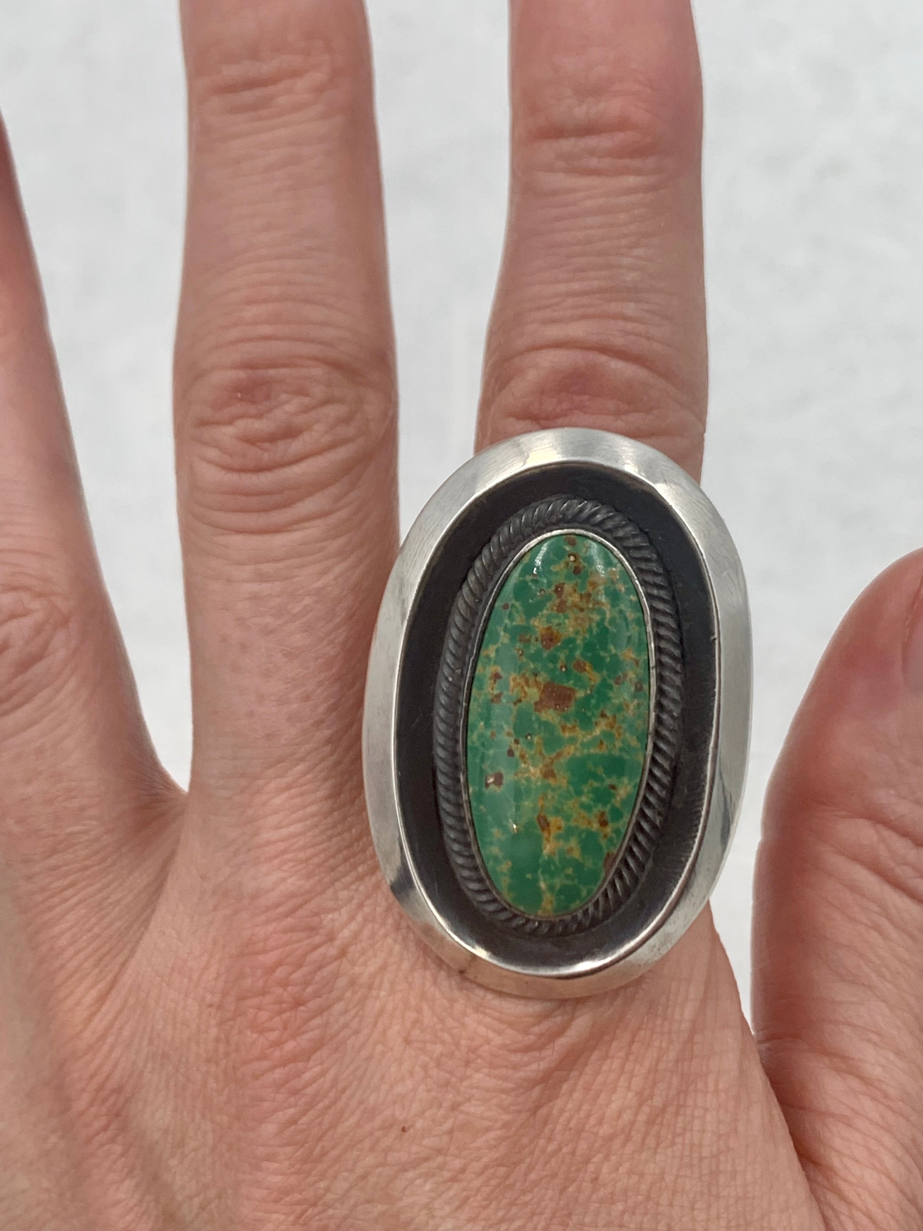 Turquoise ring created by Navajo silversmith Leon Martinez. The ring has a 1/2 inch x 1 inch green turquoise stone in a 1 inch x 1 3/4 inch contemporary sterling silver setting. 

The 1/4 inch band is adjustable from size 7 to size 13. 
Hallmark on